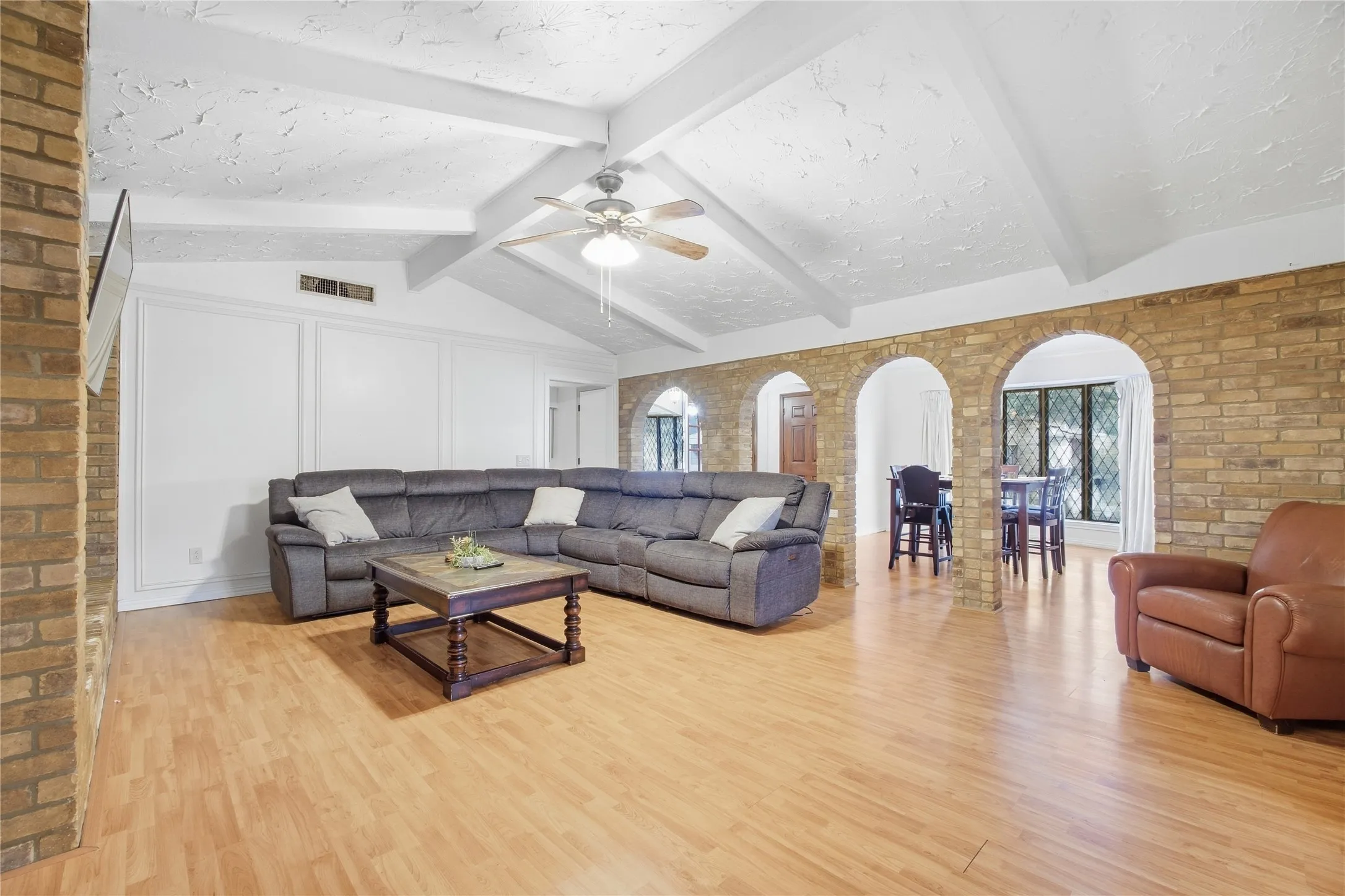 Vaulted ceiling with exposed beams, wood-finish flooring, brick archways, and paneling accent walls