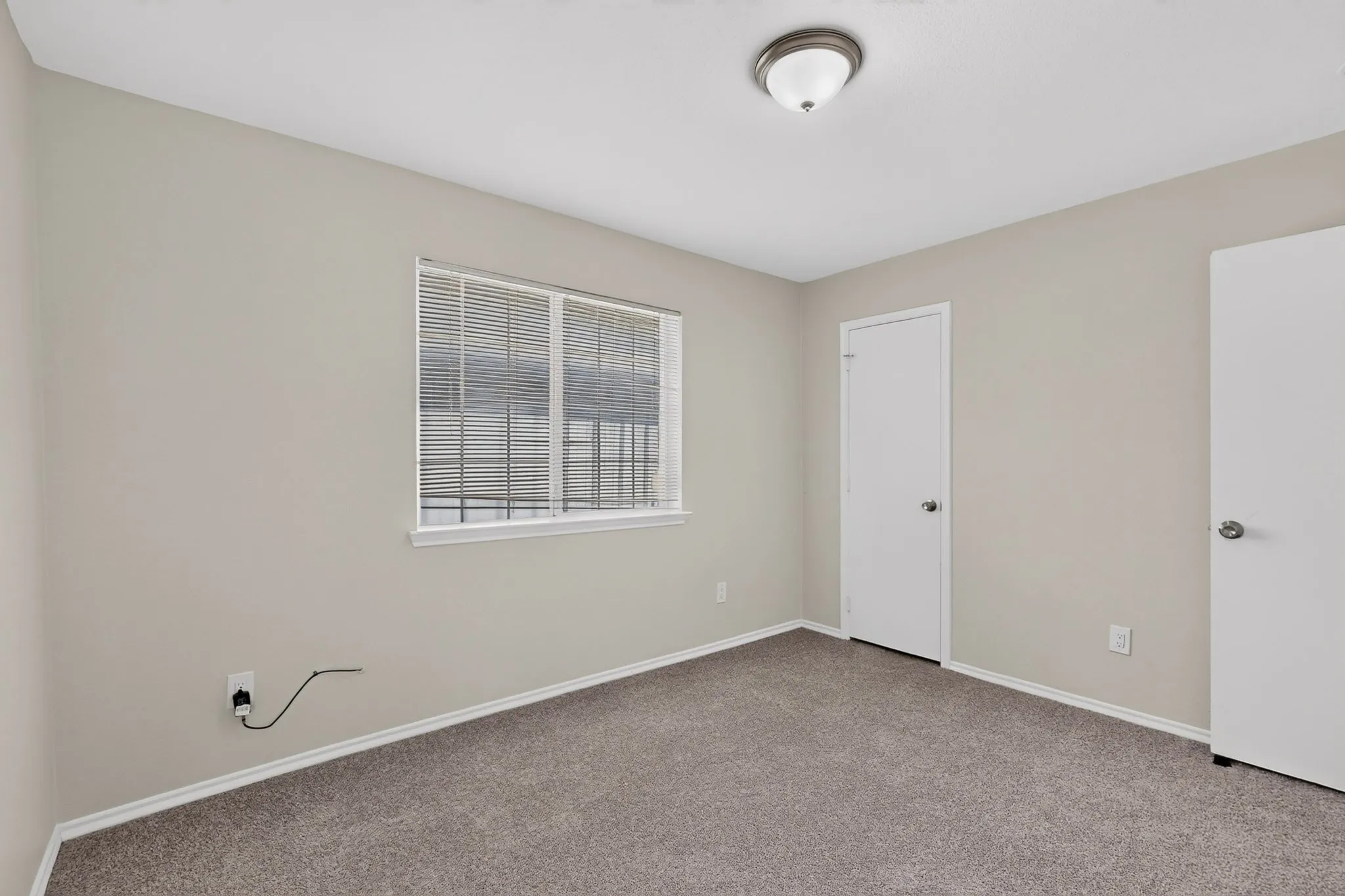 Neutral paint palette, textured carpet flooring, ceiling-mounted light fixture, and window with horizontal blinds