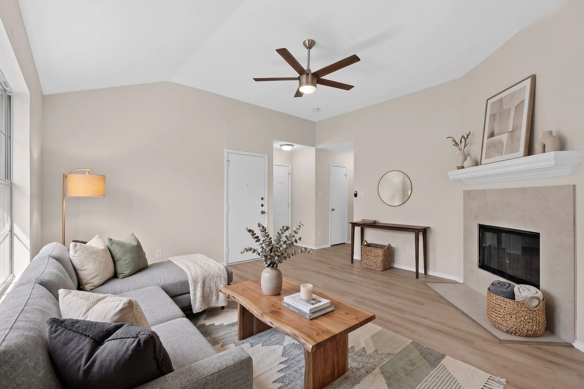 Vaulted ceilings, wood-finish flooring, a tile-surround fireplace with a white mantel, and a ceiling fan with integrated lighting