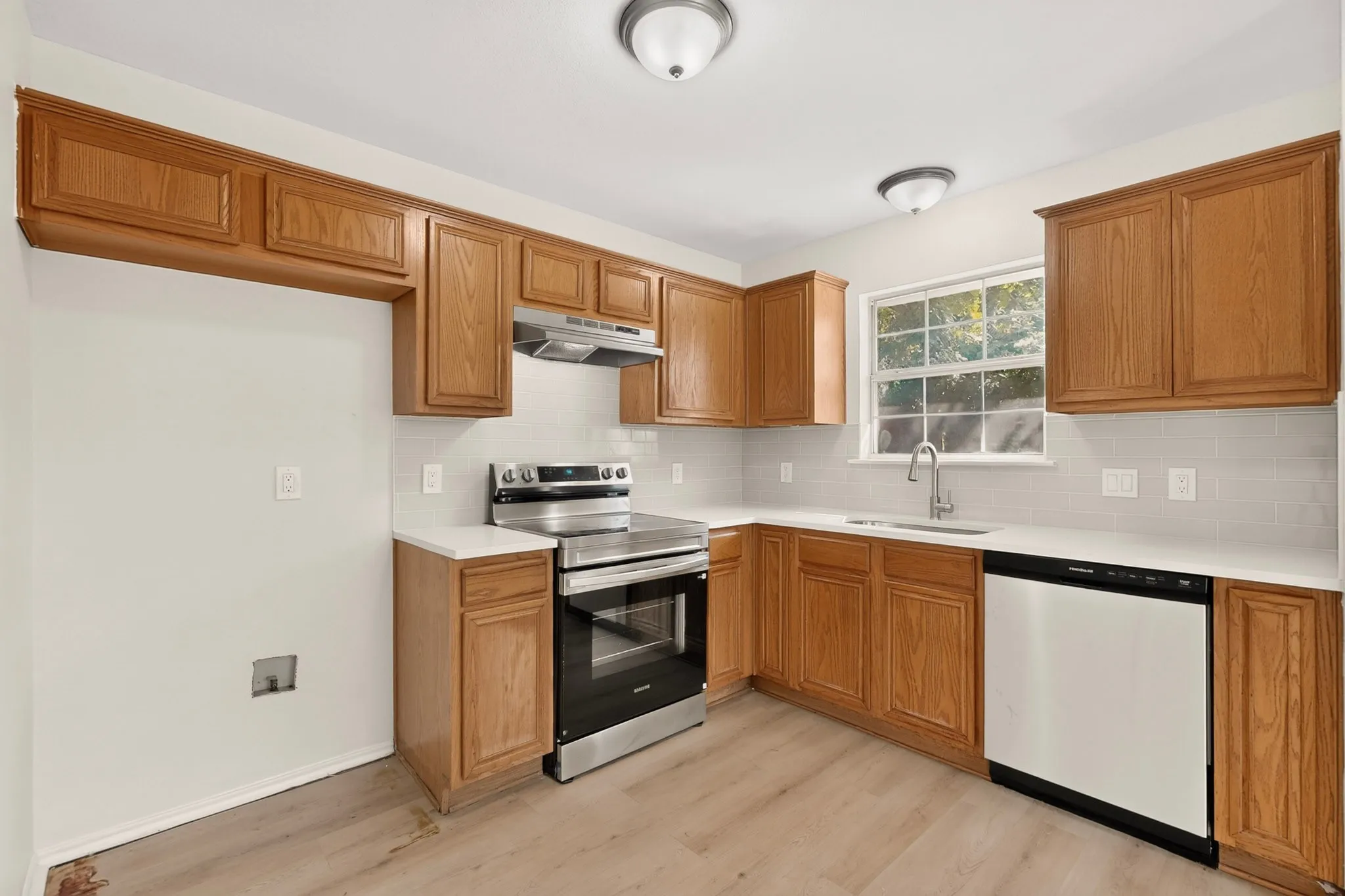 Wood-finish flooring, wood cabinetry, stainless steel range, white countertops, and subway tile backsplash