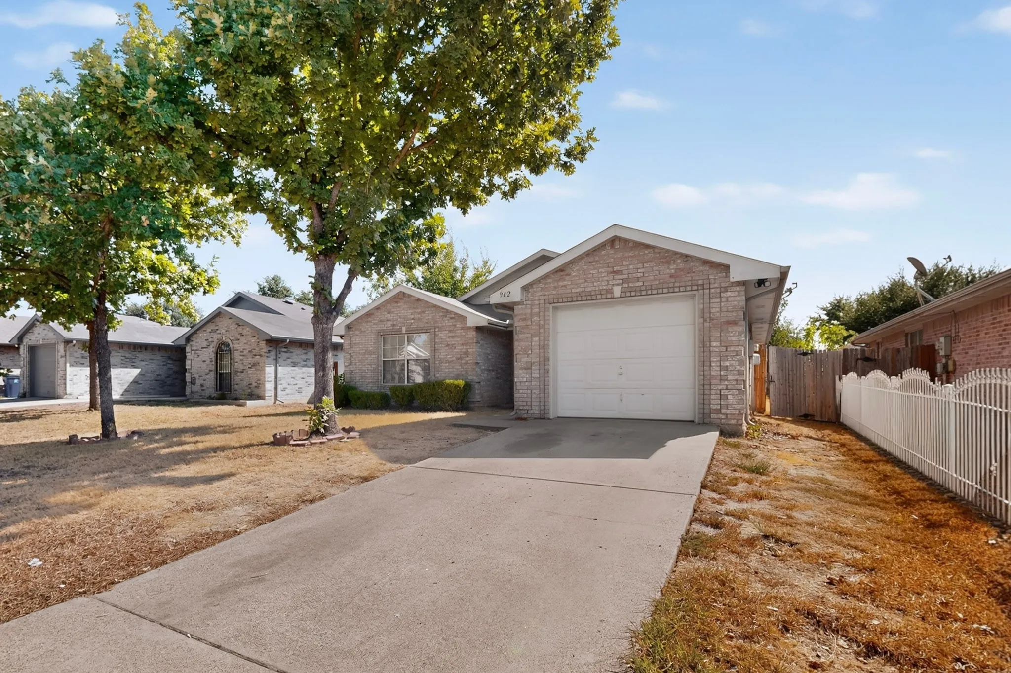 Brick exterior with an attached garage, concrete driveway, and mature trees