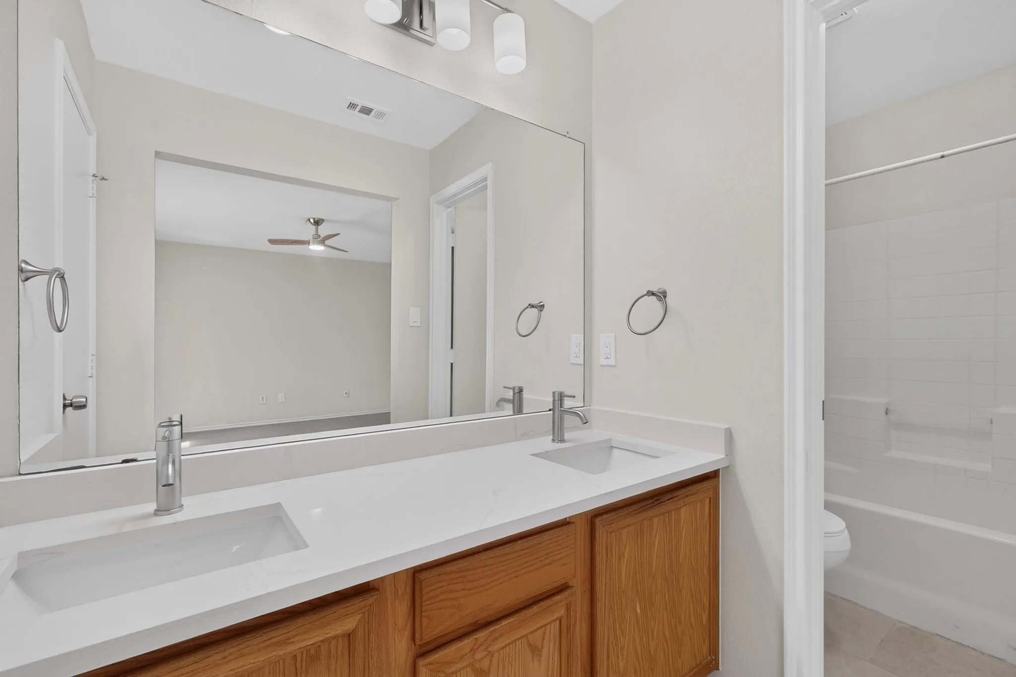 Dual vanity with integrated sinks, light-toned countertop, wood-finish cabinetry, and brushed nickel fixtures
