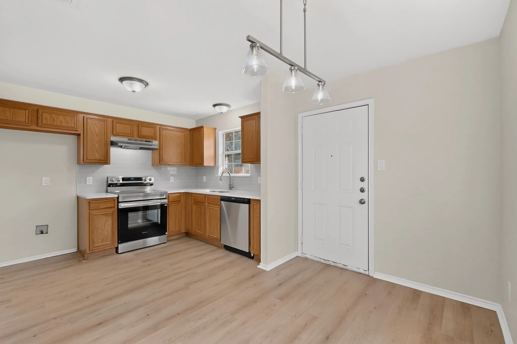 Kitchen featuring wood-finish flooring, stainless steel appliances, wood cabinetry, white countertops, and a subway tile backsplash