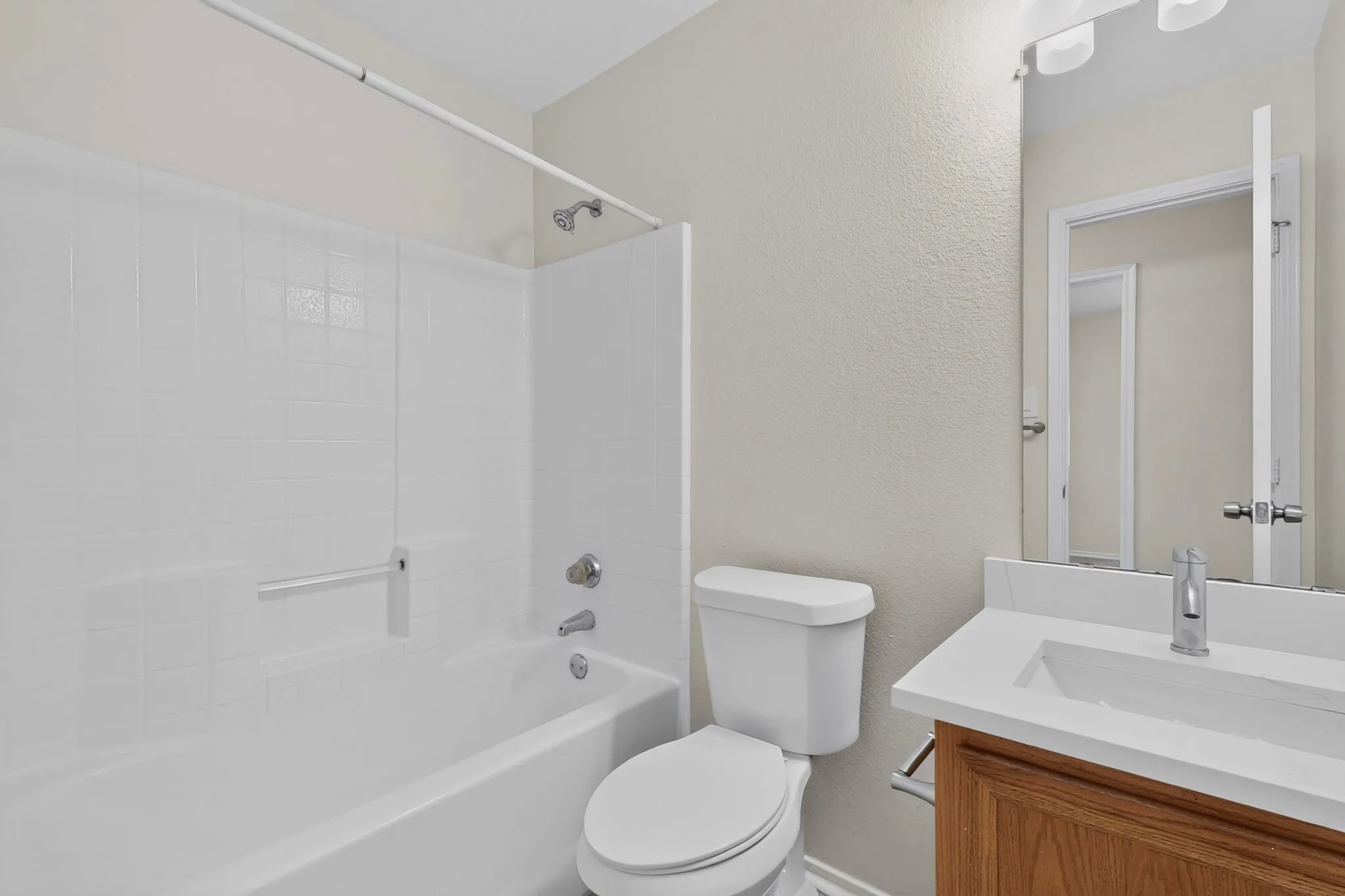 Bathroom featuring a white bathtub with tile surround, toilet, vanity with integrated sink, and wall-mounted mirror with overhead lighting