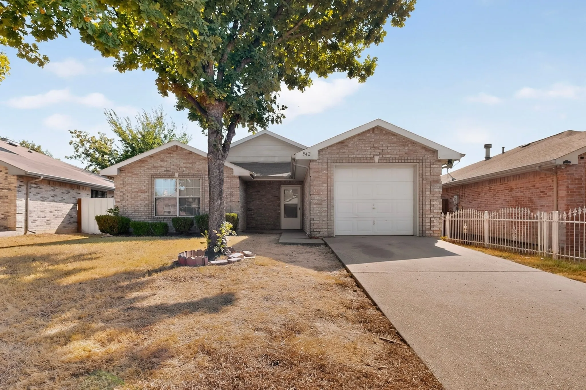 Brick exterior, attached garage, mature tree, concrete driveway, and front landscaping