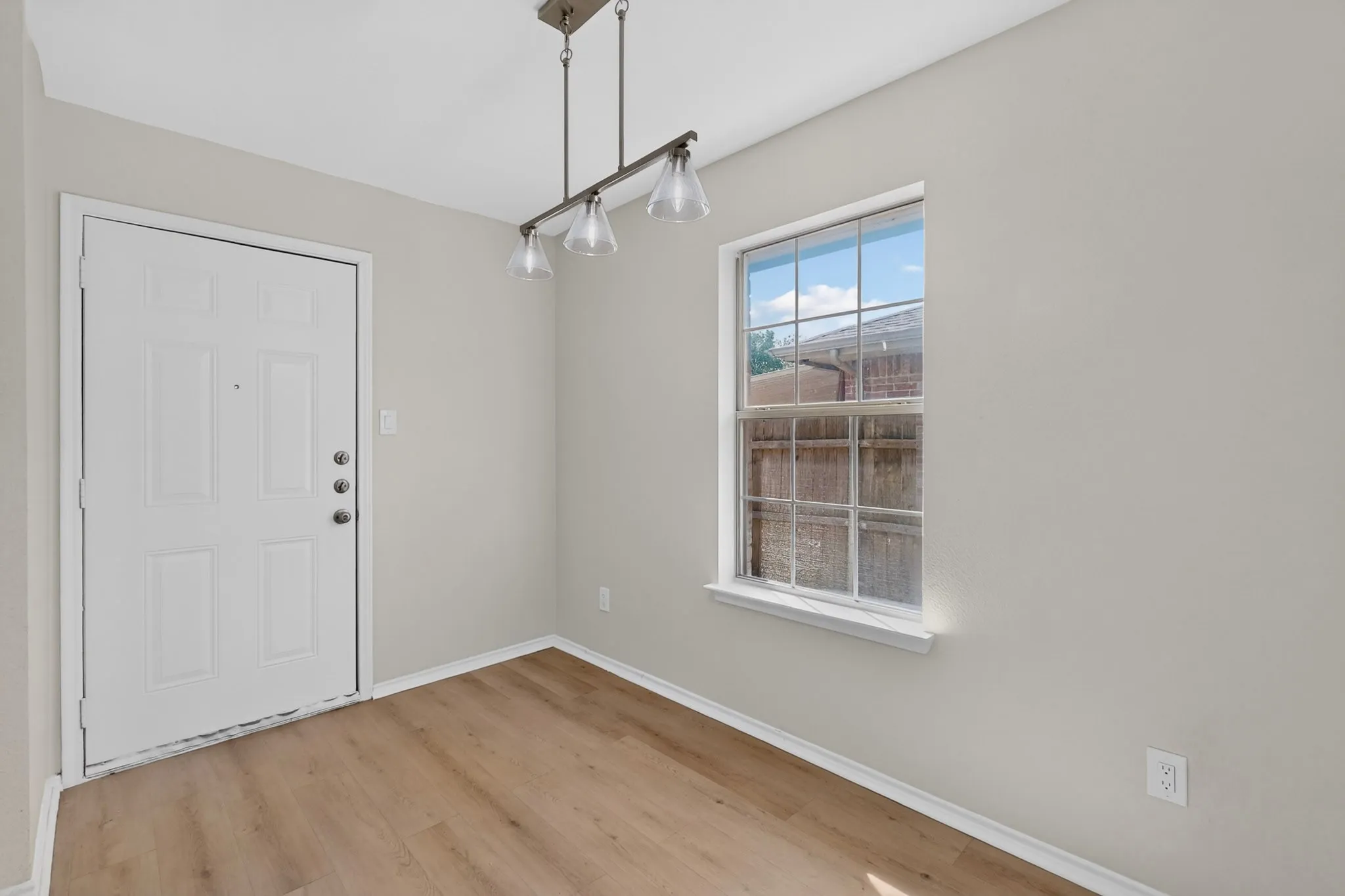 Wood-finish flooring, white paneled door, multi-light linear chandelier, and a double-hung window