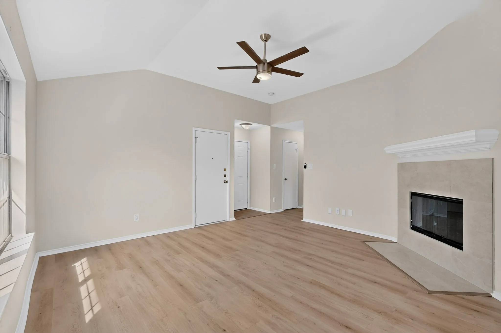 Vaulted ceiling with a ceiling fan, wood-finish flooring, and a fireplace with a mantel