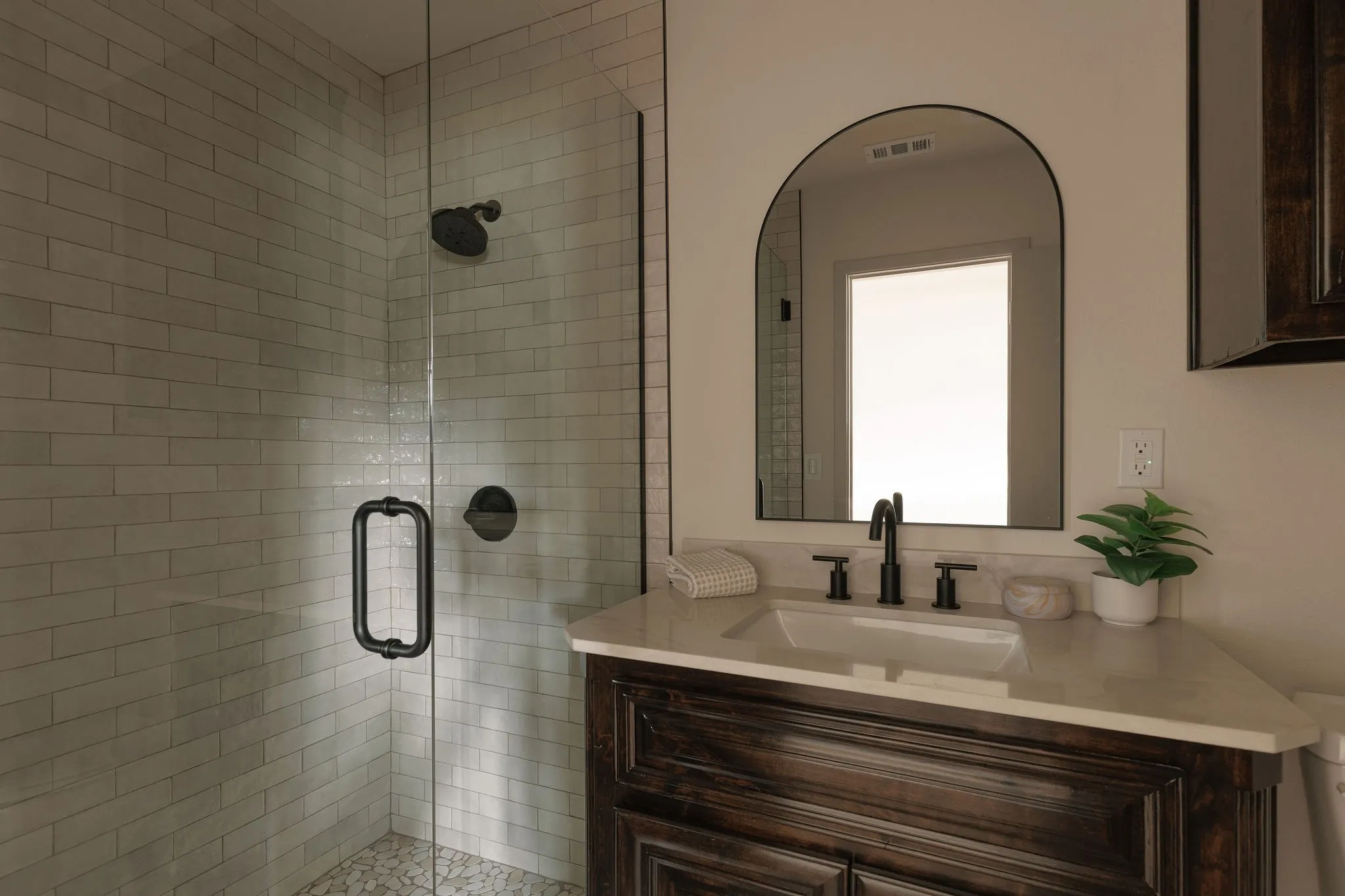 A thoughtfully updated secondary bath with warm wood tones, textural tile and contrasting matte black fixtures.