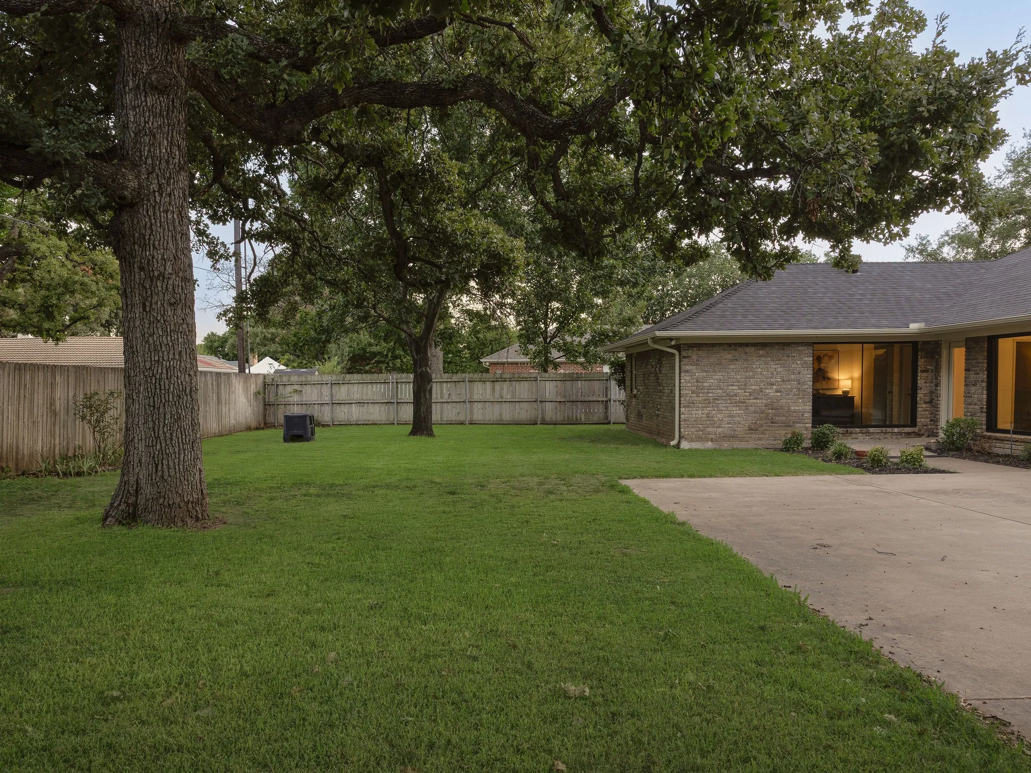 The rear exterior highlights the home’s expansive storefront windows, established trees and generous backyard.