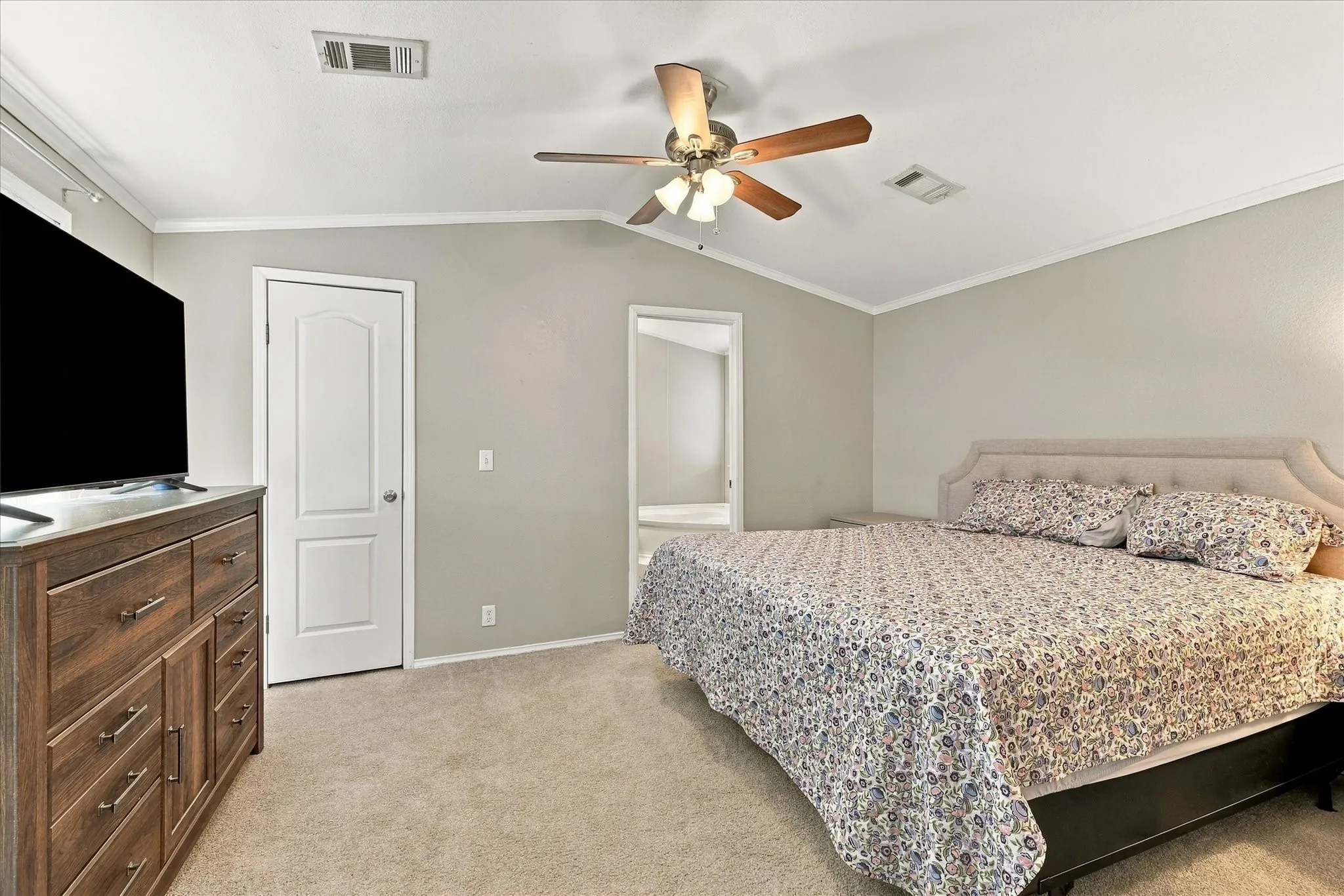 Vaulted ceiling with a ceiling fan, crown molding, light neutral wall paint, and carpeting