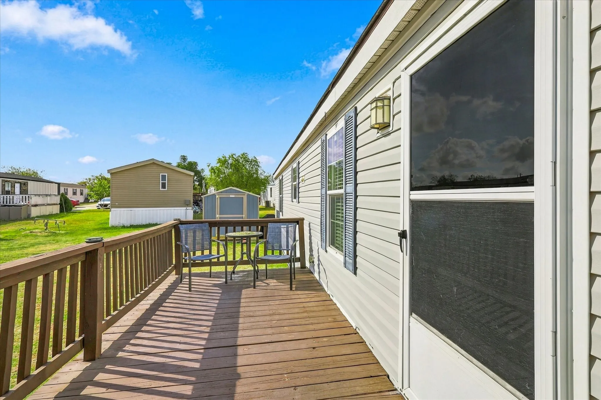 Wood-finish deck with railing, light-colored exterior siding, and outdoor wall-mounted lighting