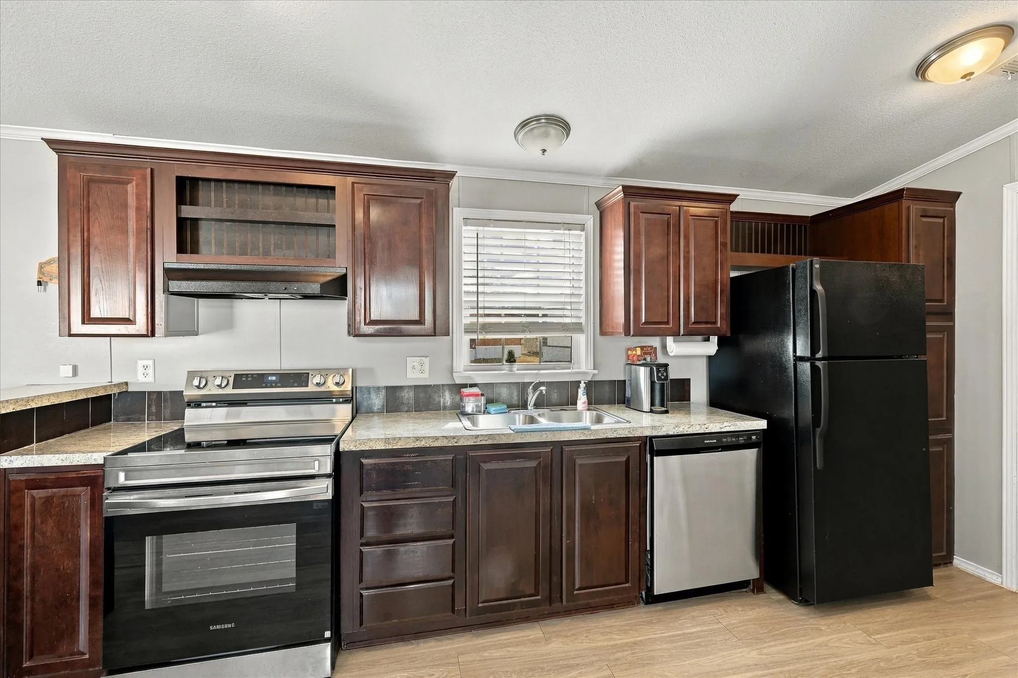 Kitchen featuring wood-finish flooring, dark wood cabinetry, stainless steel range, stainless steel dishwasher, and a black refrigerator