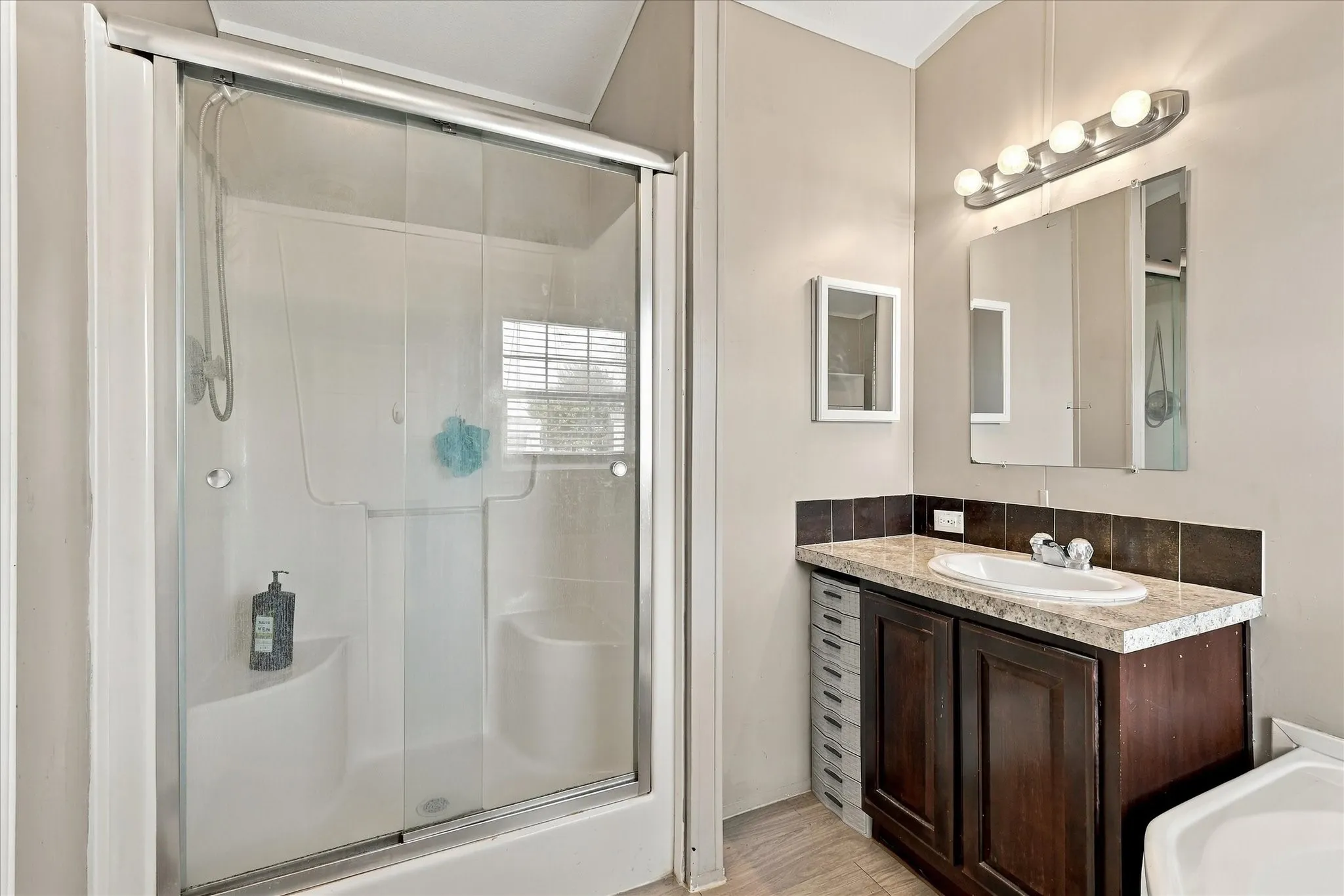 Enclosed shower with sliding glass doors, built-in seating, wood-finish vanity with an integrated sink, and an overhead vanity light fixture