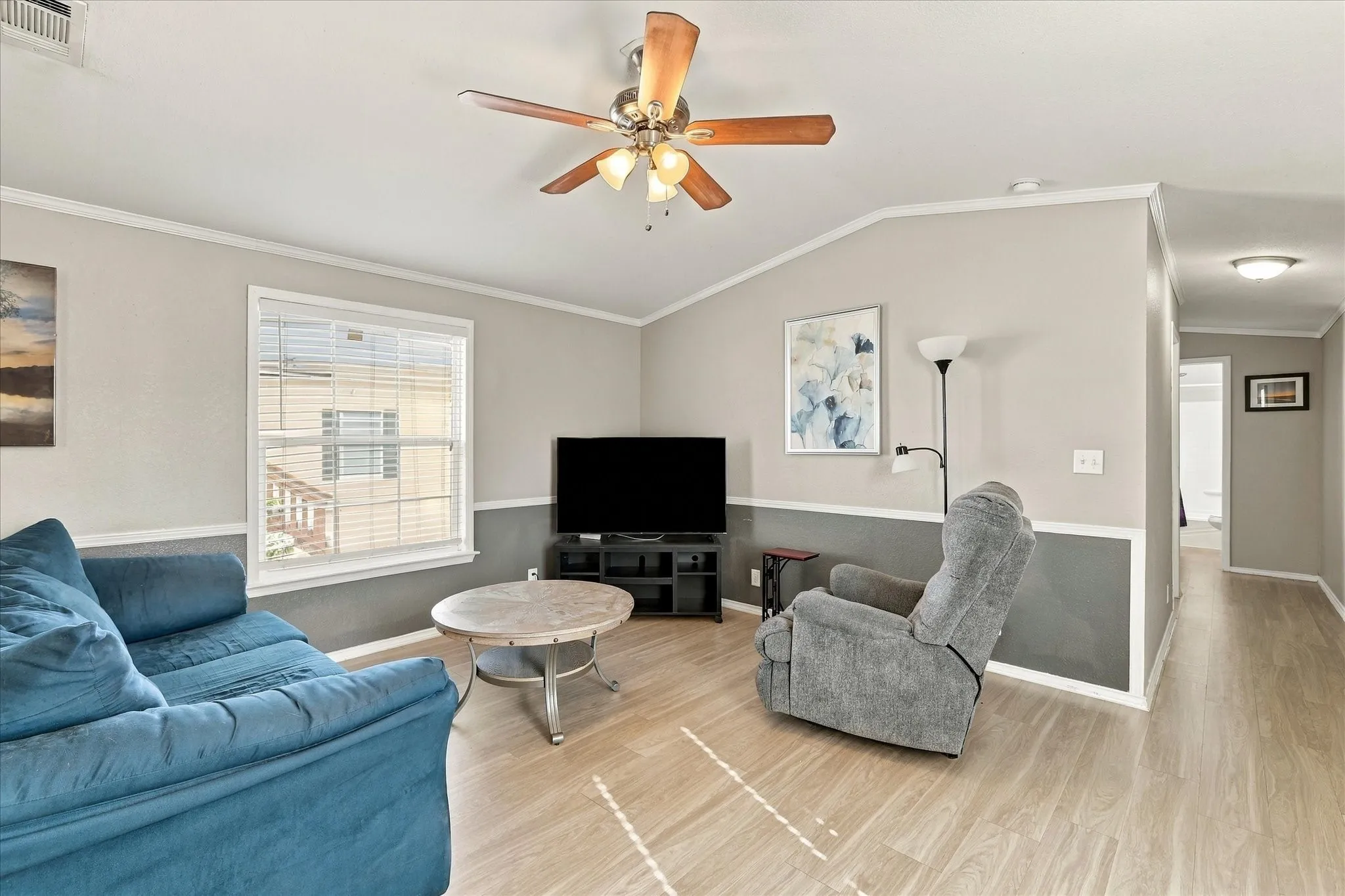 Vaulted ceiling with a ceiling fan, light wood-finish flooring, two-tone wall treatment, and a window with blinds