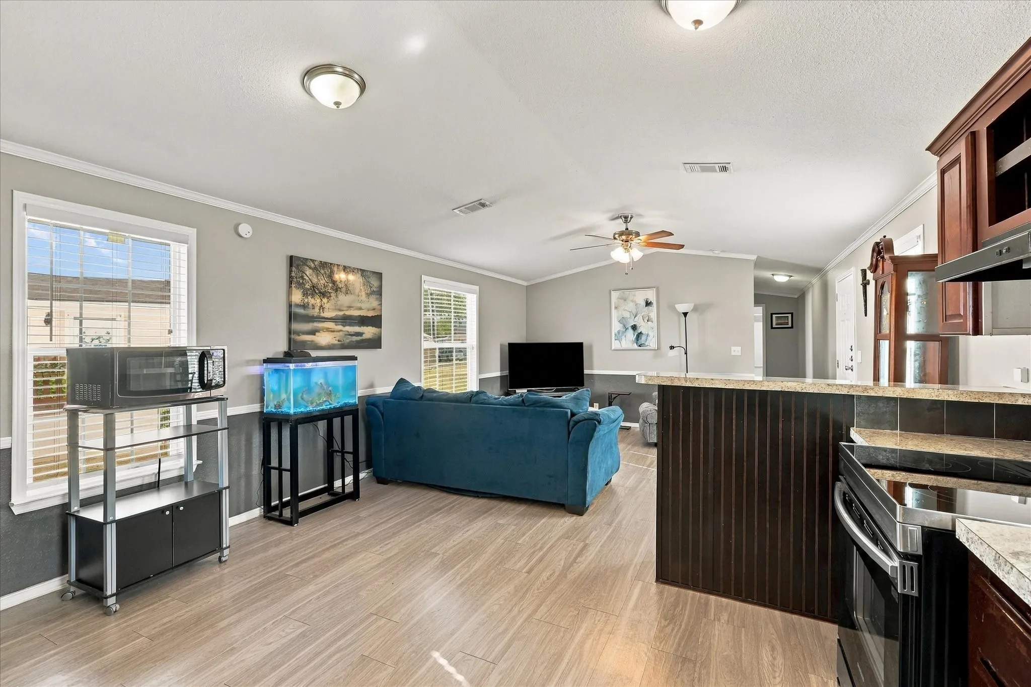 Open-concept living area with wood-finish flooring, a kitchen island featuring beadboard paneling, and an electric stove with an overhead microwave