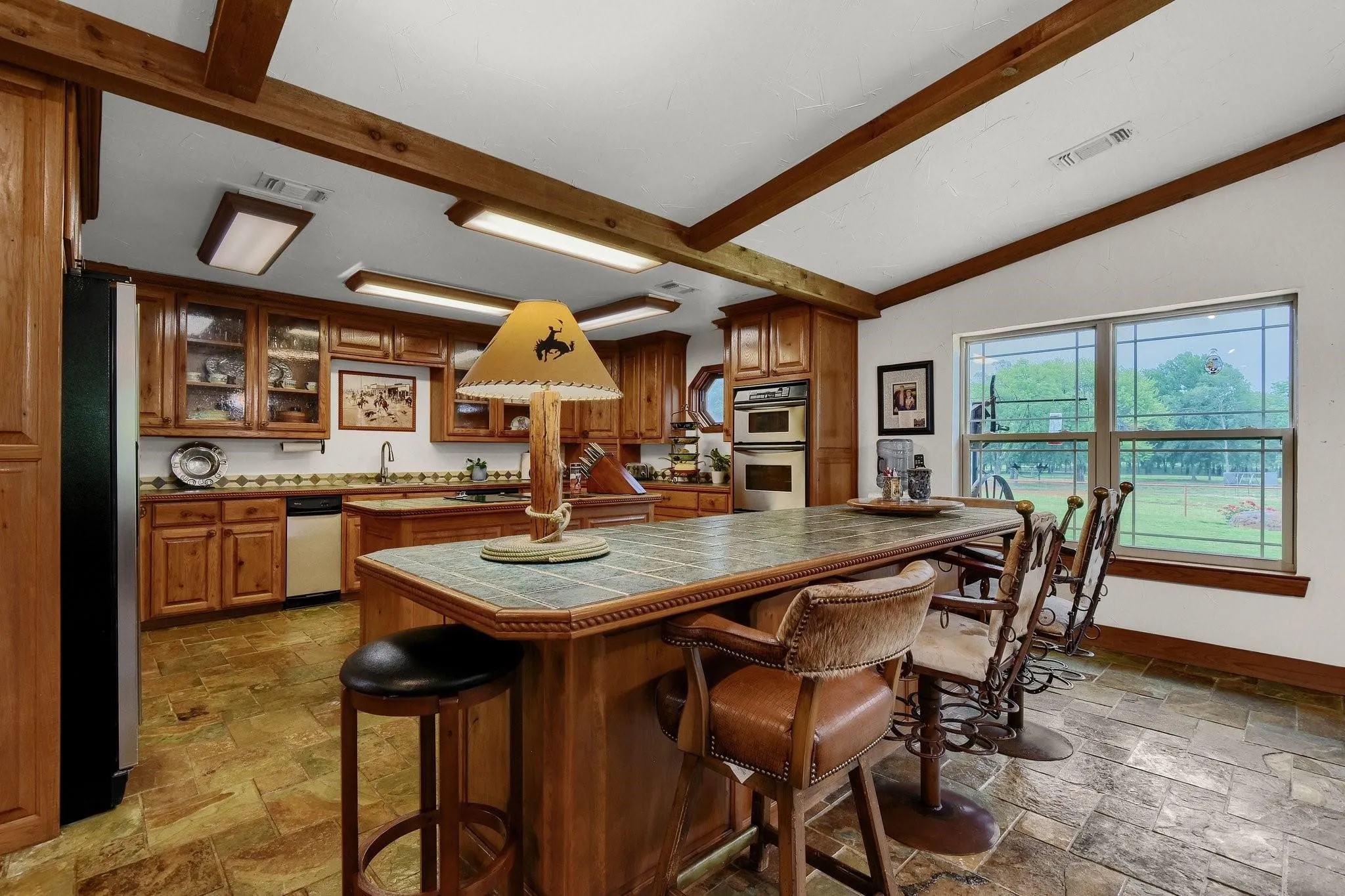 Kitchen with a breakfast bar area, brown cabinetry, glass insert cabinets, tile countertops, and a kitchen island