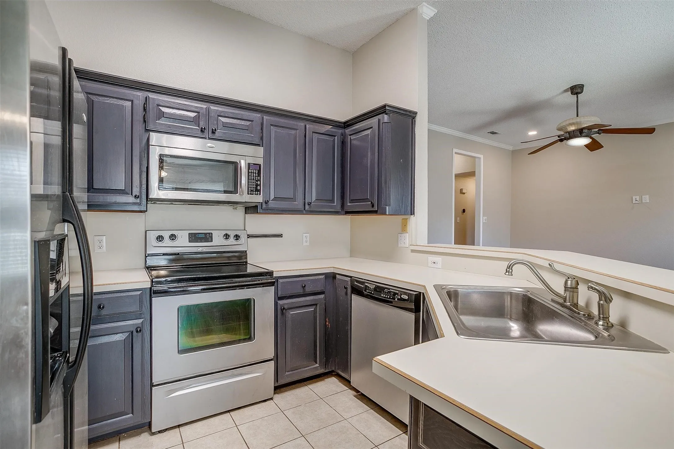 Kitchen featuring stainless steel appliances, dark wood-finish cabinetry, light-toned countertops, and a double basin sink