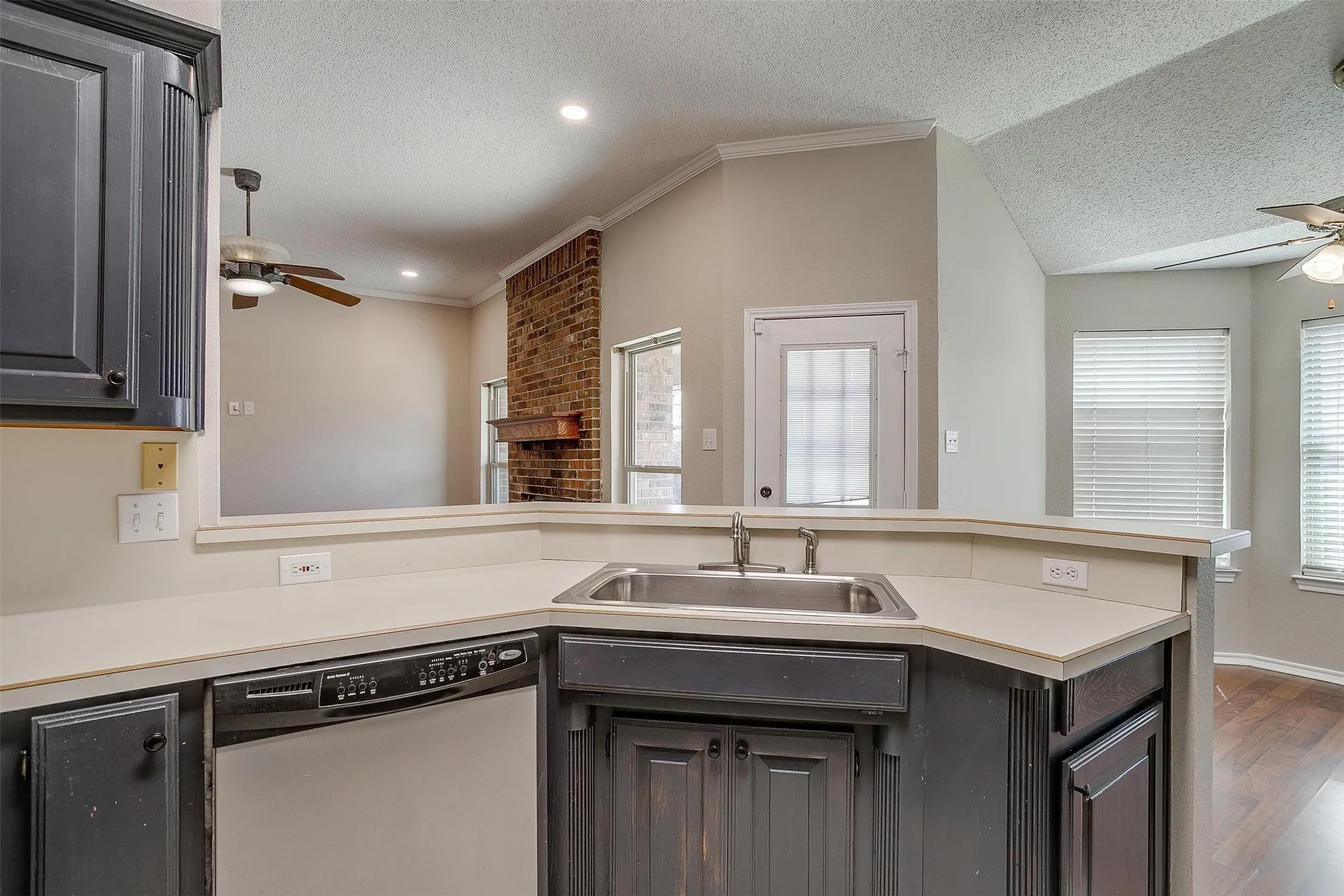 Kitchen with dark wood-finish cabinetry, built-in dishwasher, stainless steel sink with coordinating faucet, and light-toned countertops