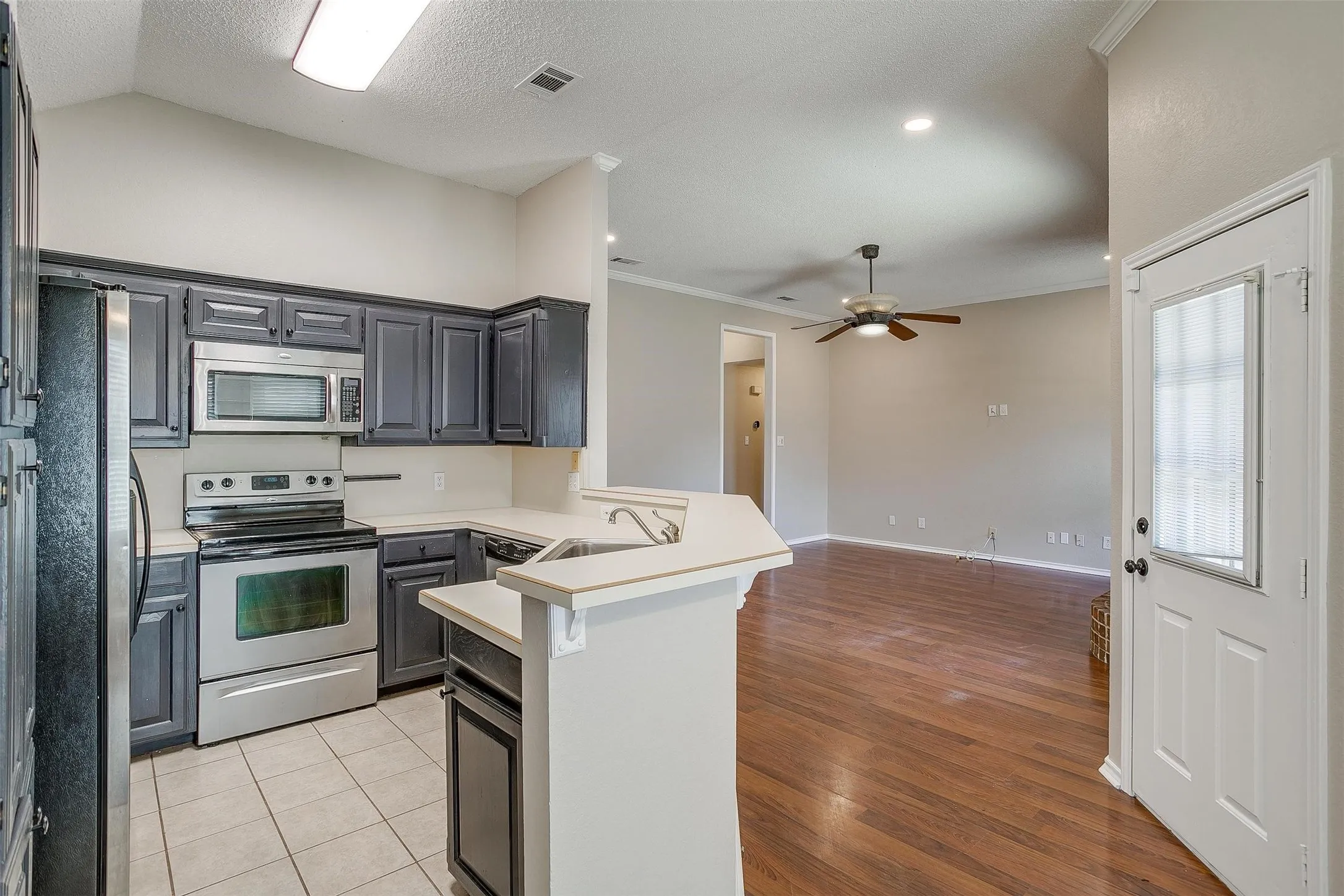 Kitchen featuring stainless steel appliances, dark wood-finish cabinetry, and light tile flooring
