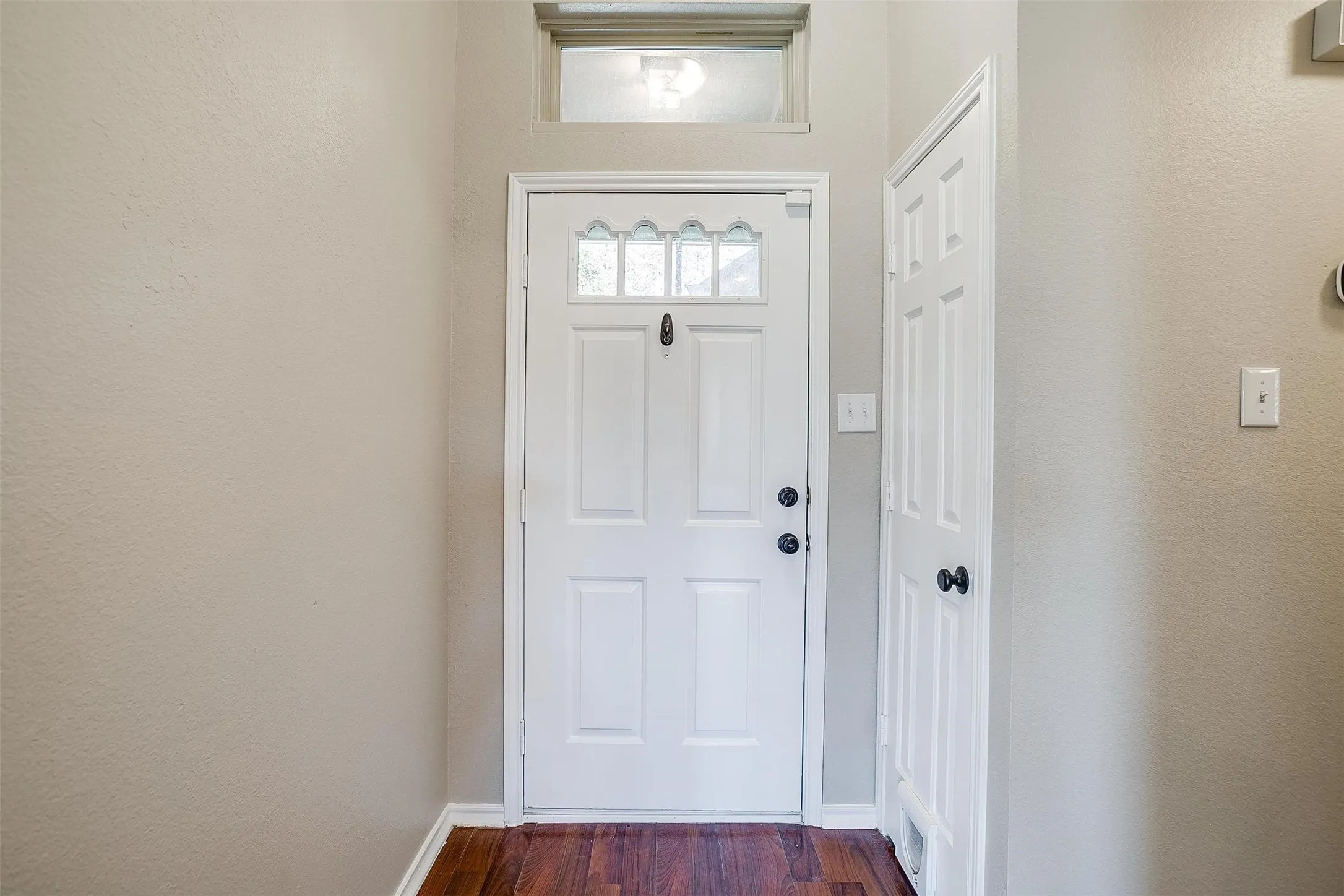 White paneled entry door with decorative glass inserts, transom window, and wood-finish flooring