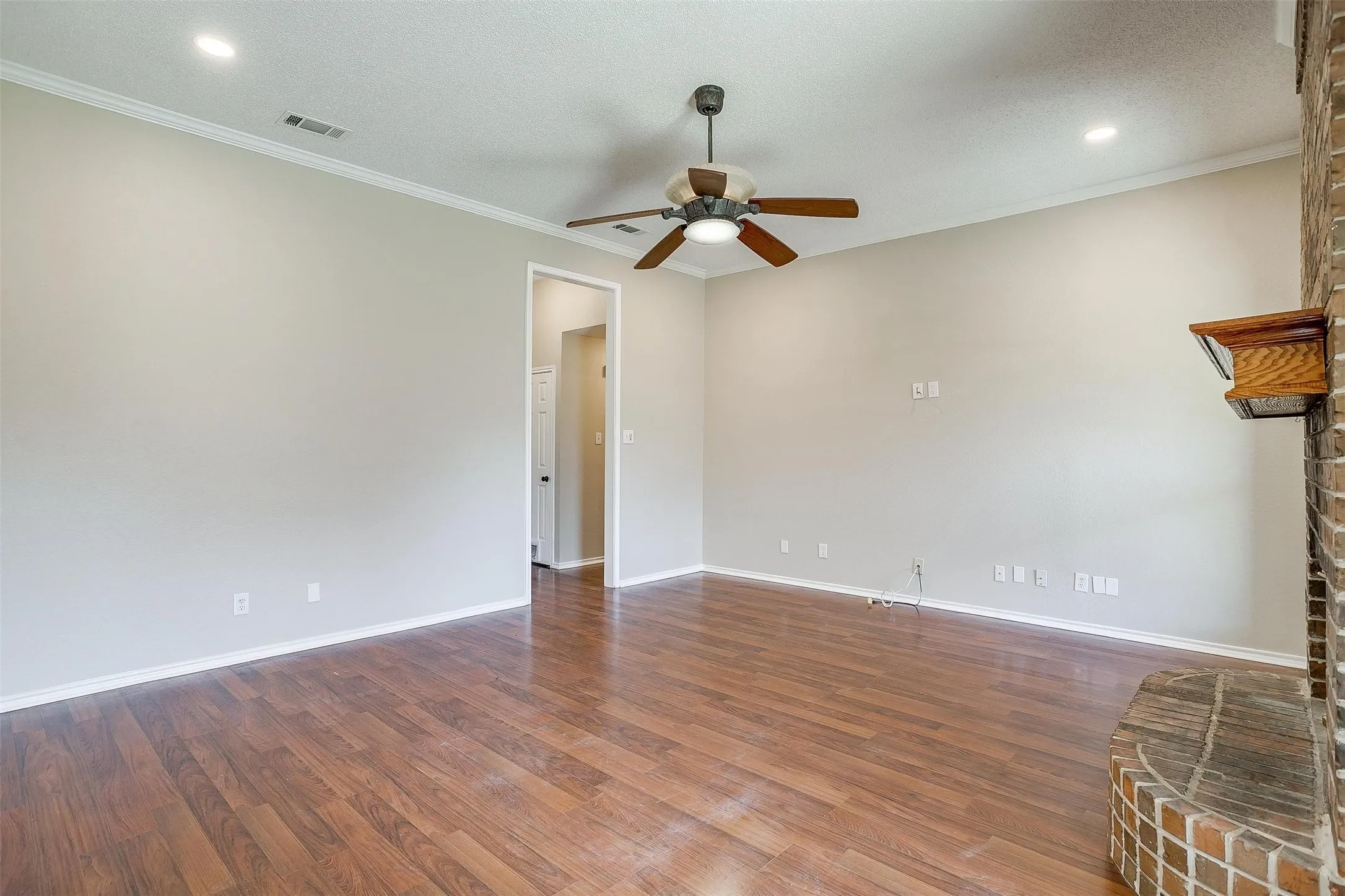 Wood-finish flooring, recessed lighting, ceiling fan, crown molding, and a brick fireplace with a wood mantle