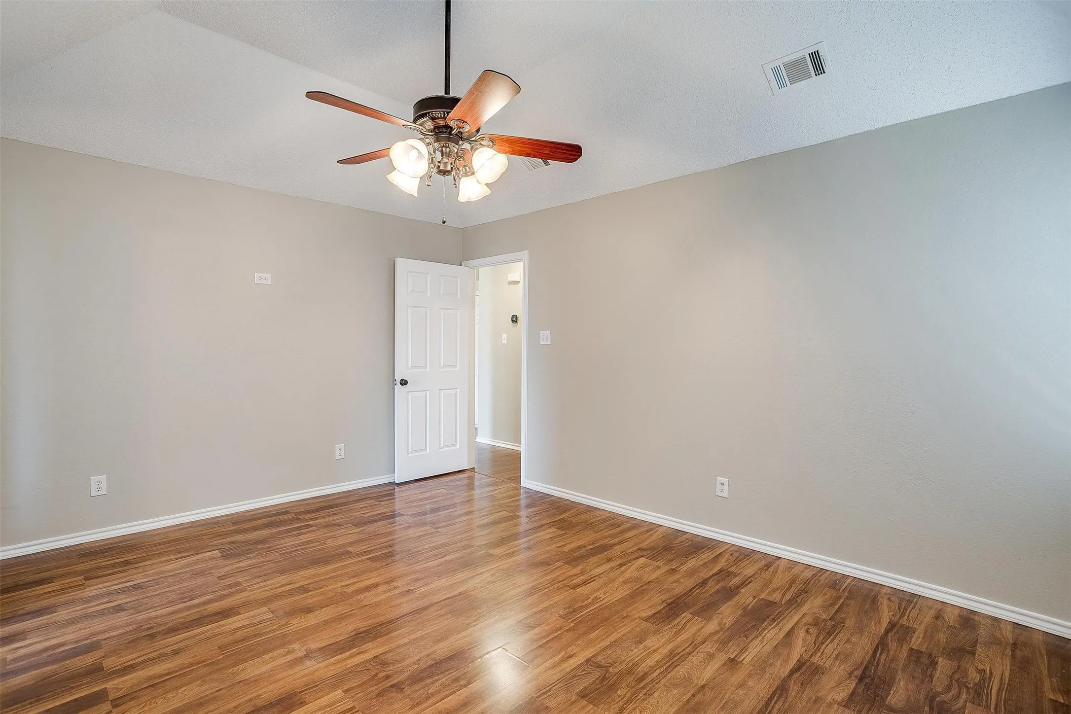 Wood-finish flooring, neutral wall tones, ceiling fan with integrated lighting, and white paneled interior doors