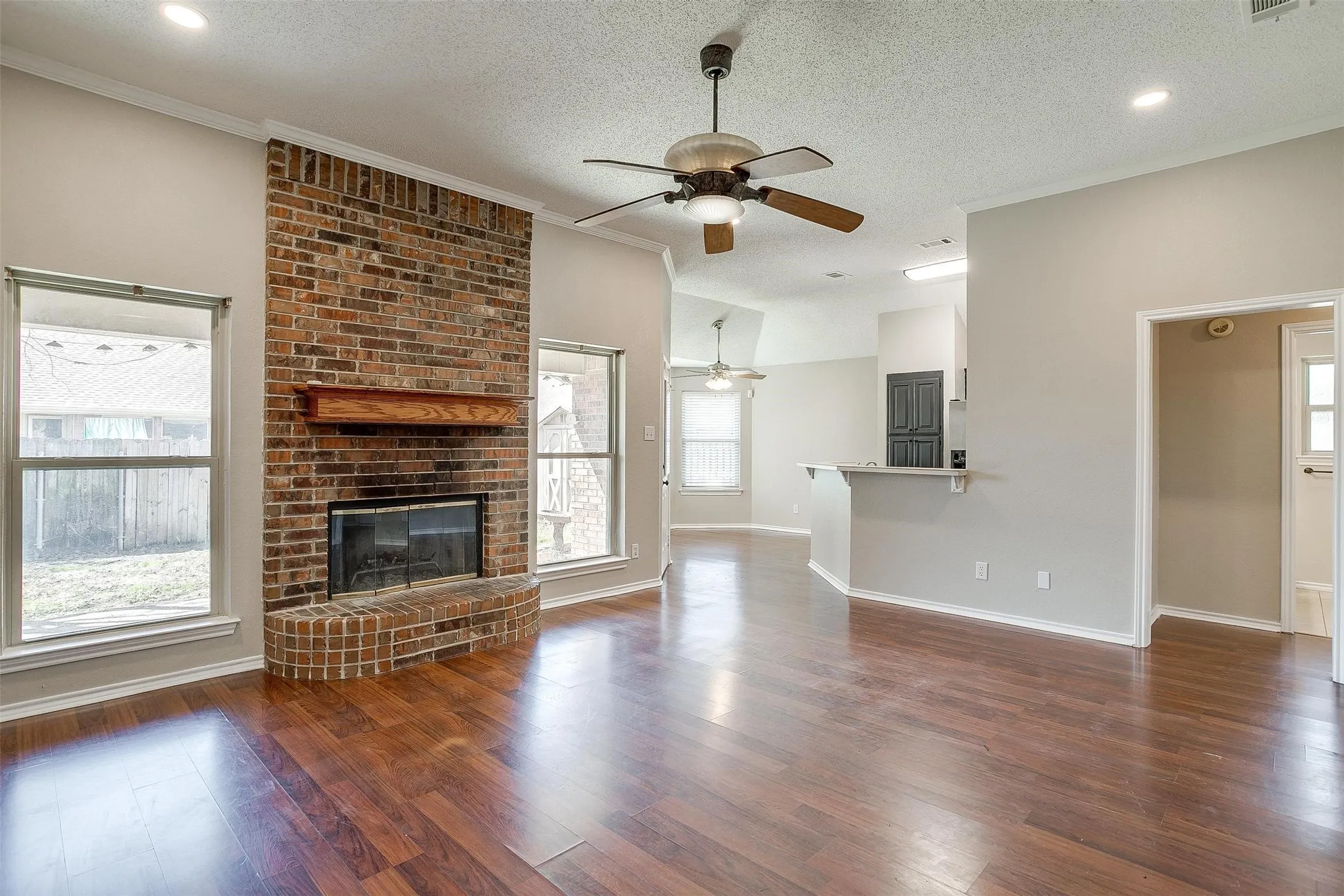 Living area featuring a brick fireplace, wood-finish flooring, vaulted ceilings, and a ceiling fan
