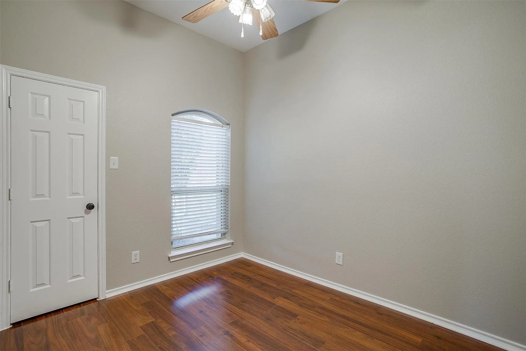 Vaulted ceiling, wood-finish flooring, arched window with blinds, panel door, and ceiling fan