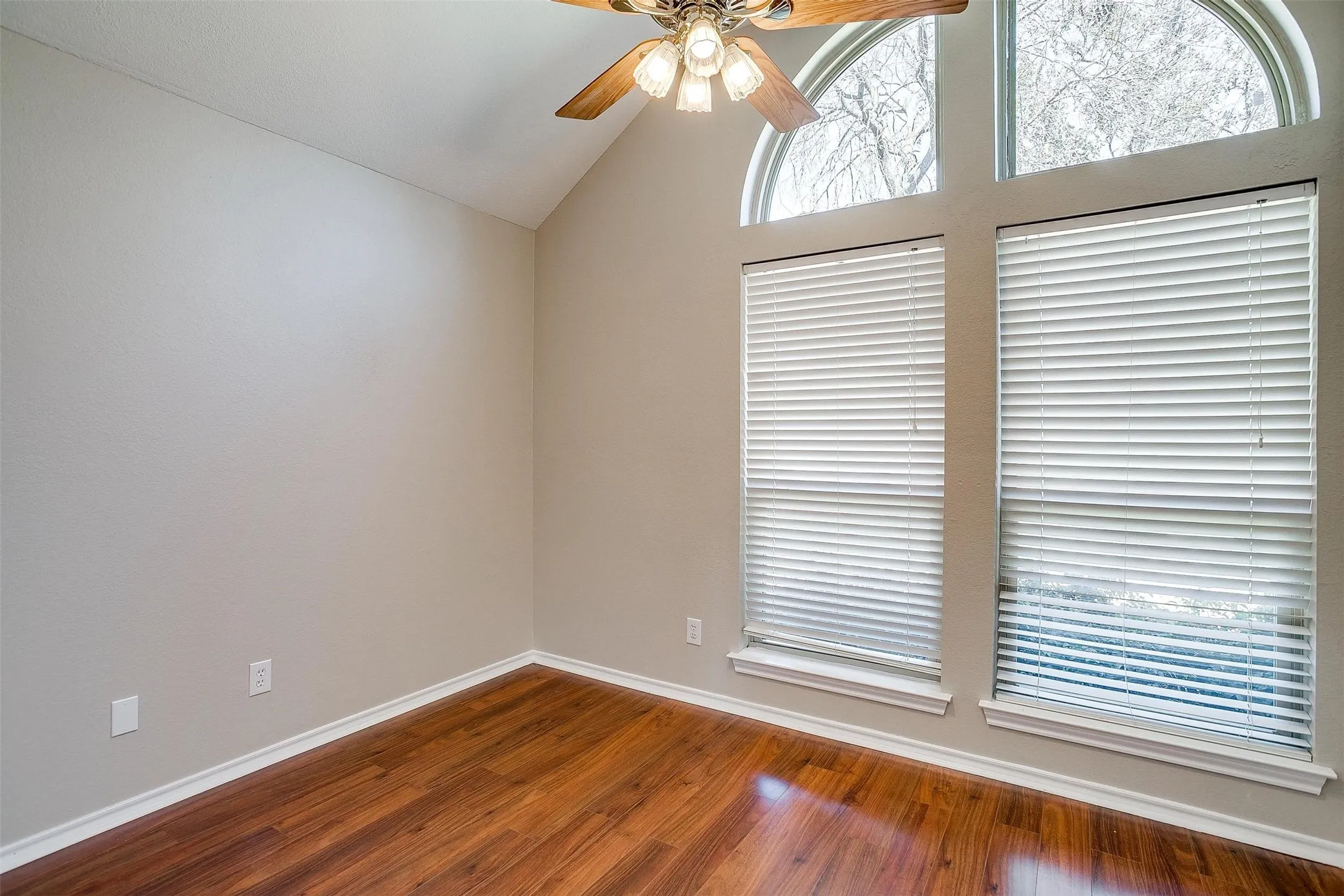 Vaulted ceiling with a ceiling fan, wood-finish flooring, and multiple windows with arched transoms