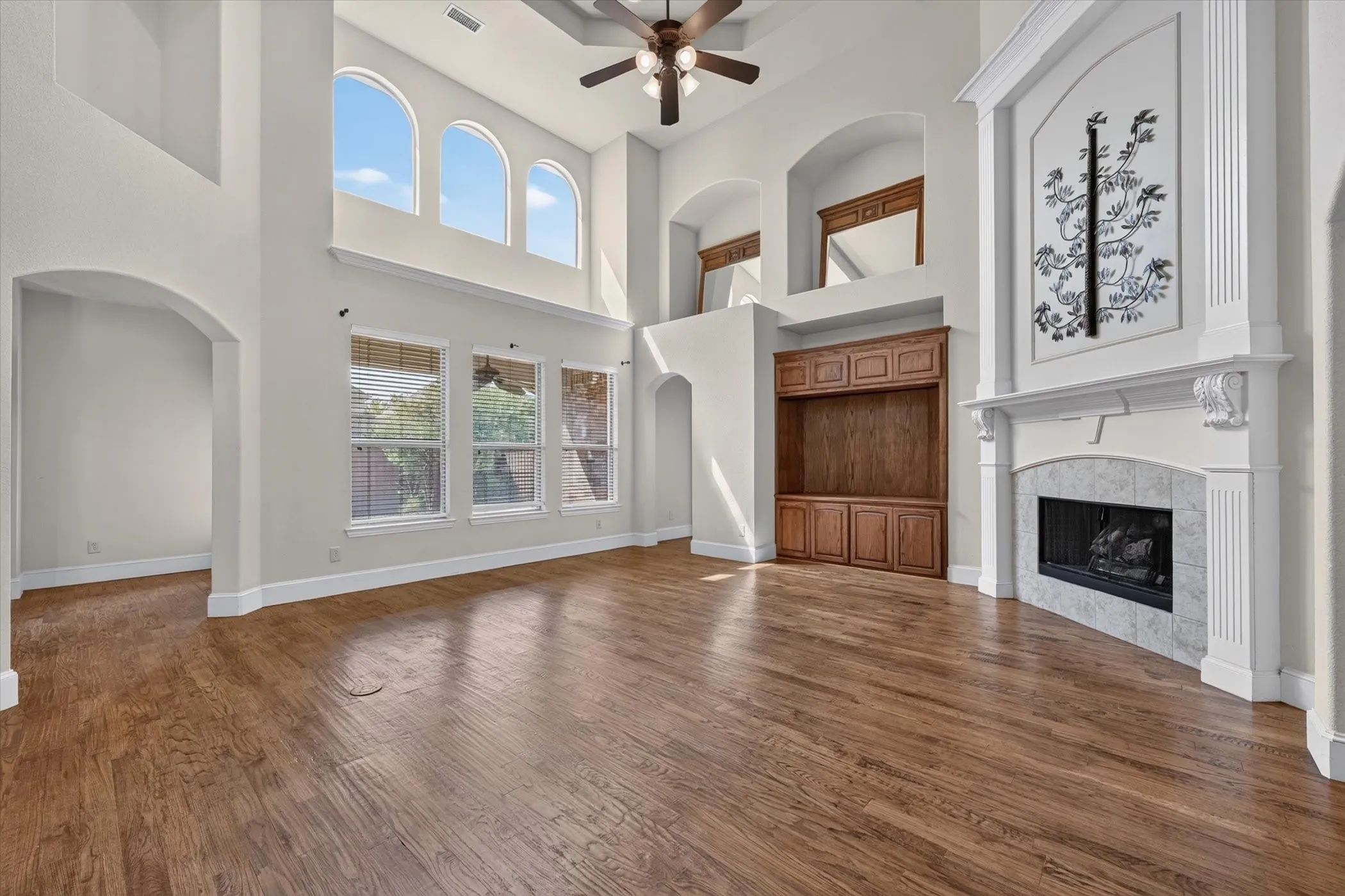 Double-height living space featuring wood-finish flooring, a built-in media cabinet, and a fireplace with a stone surround