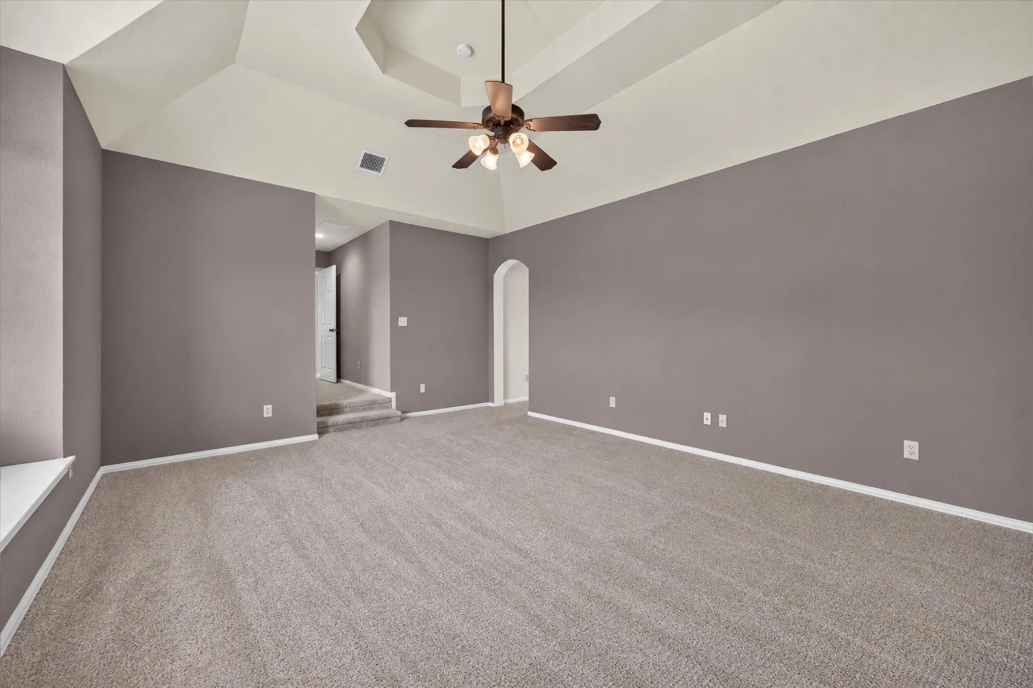 Tray ceiling with a ceiling fan light fixture, arched doorway, and carpet flooring