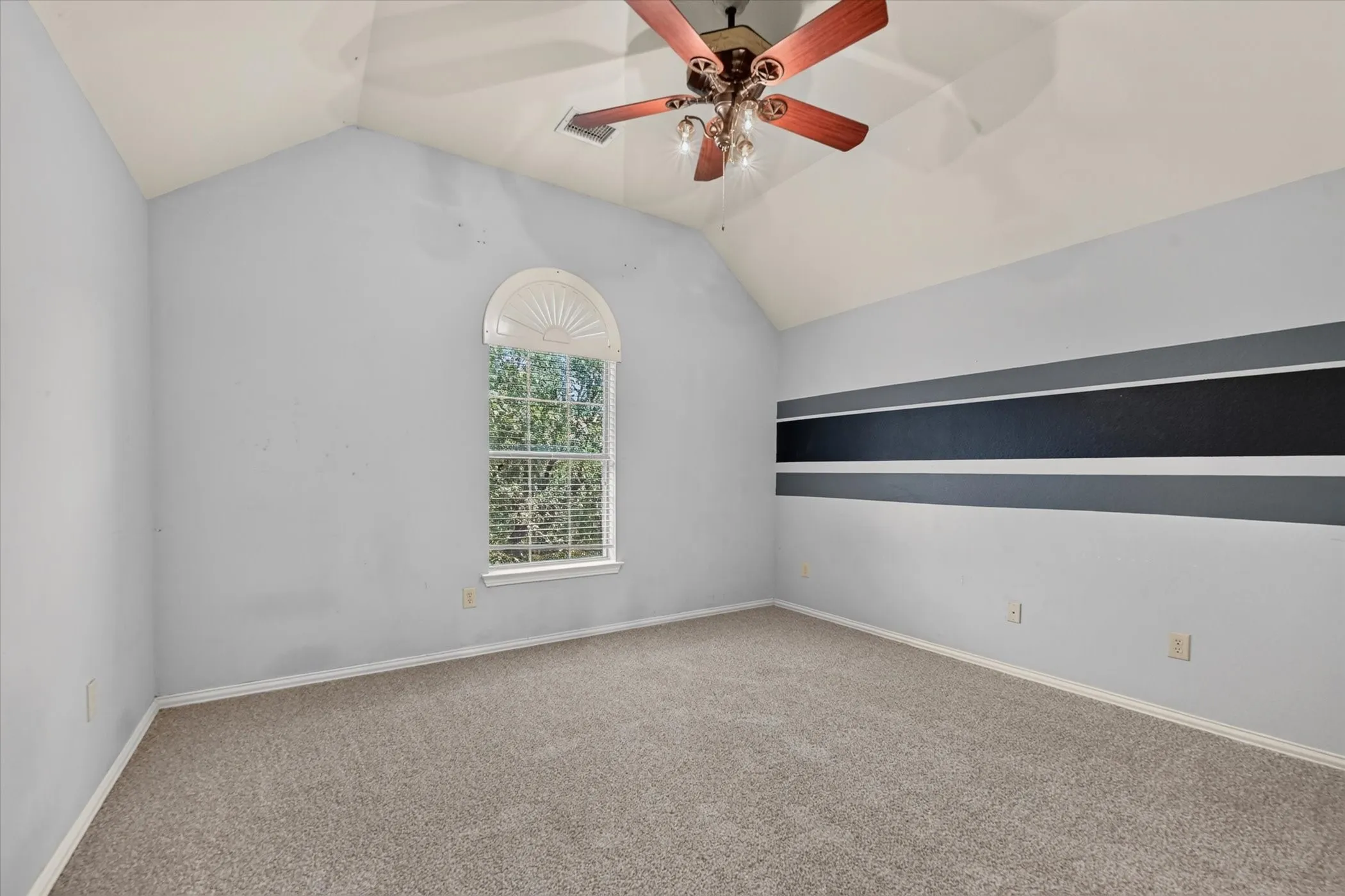 Vaulted ceiling with a ceiling fan, arched window, and carpeted flooring