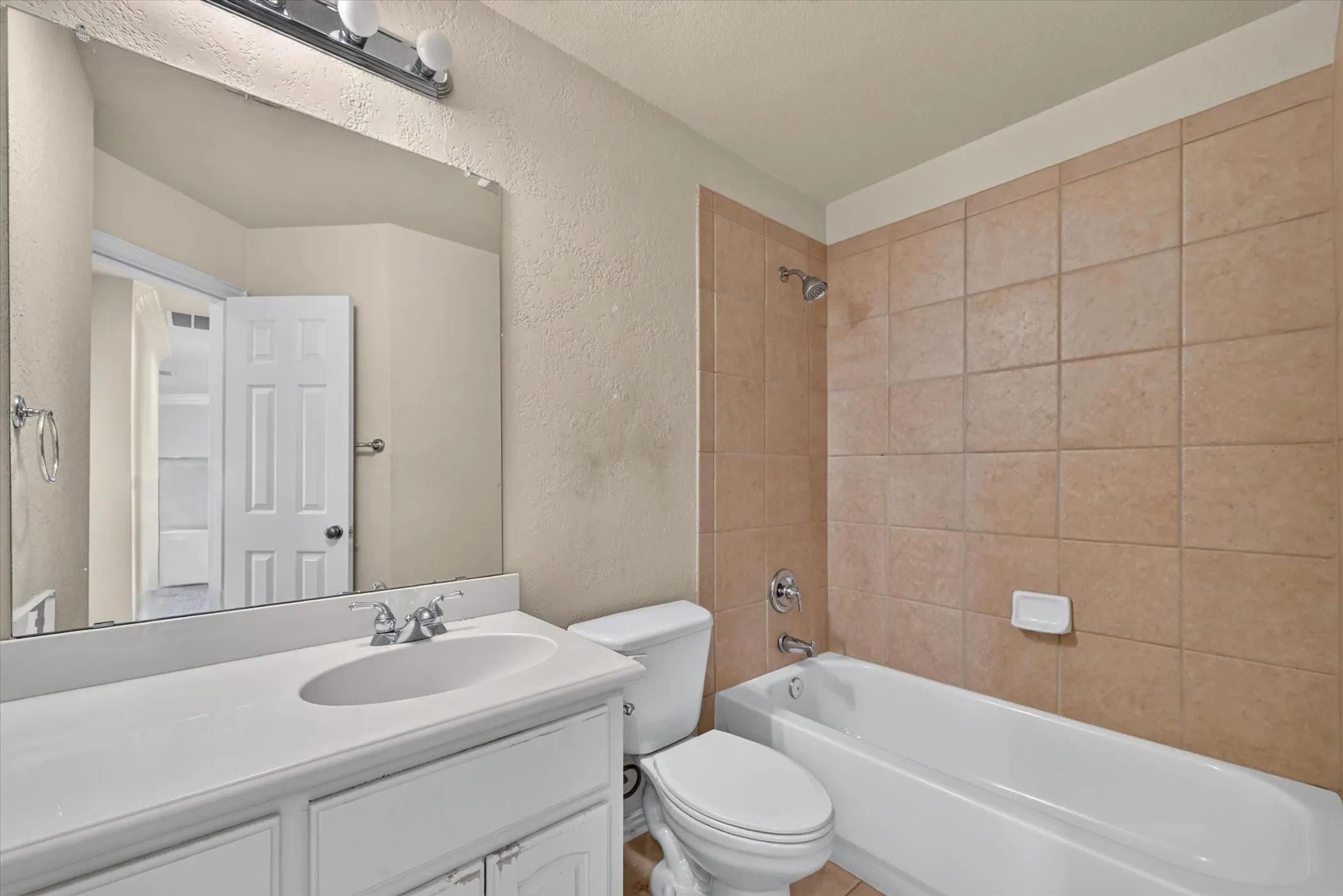 Bathroom featuring a single vanity with an integrated sink, chrome faucet, wall-mounted mirror, and a bathtub with tile surround