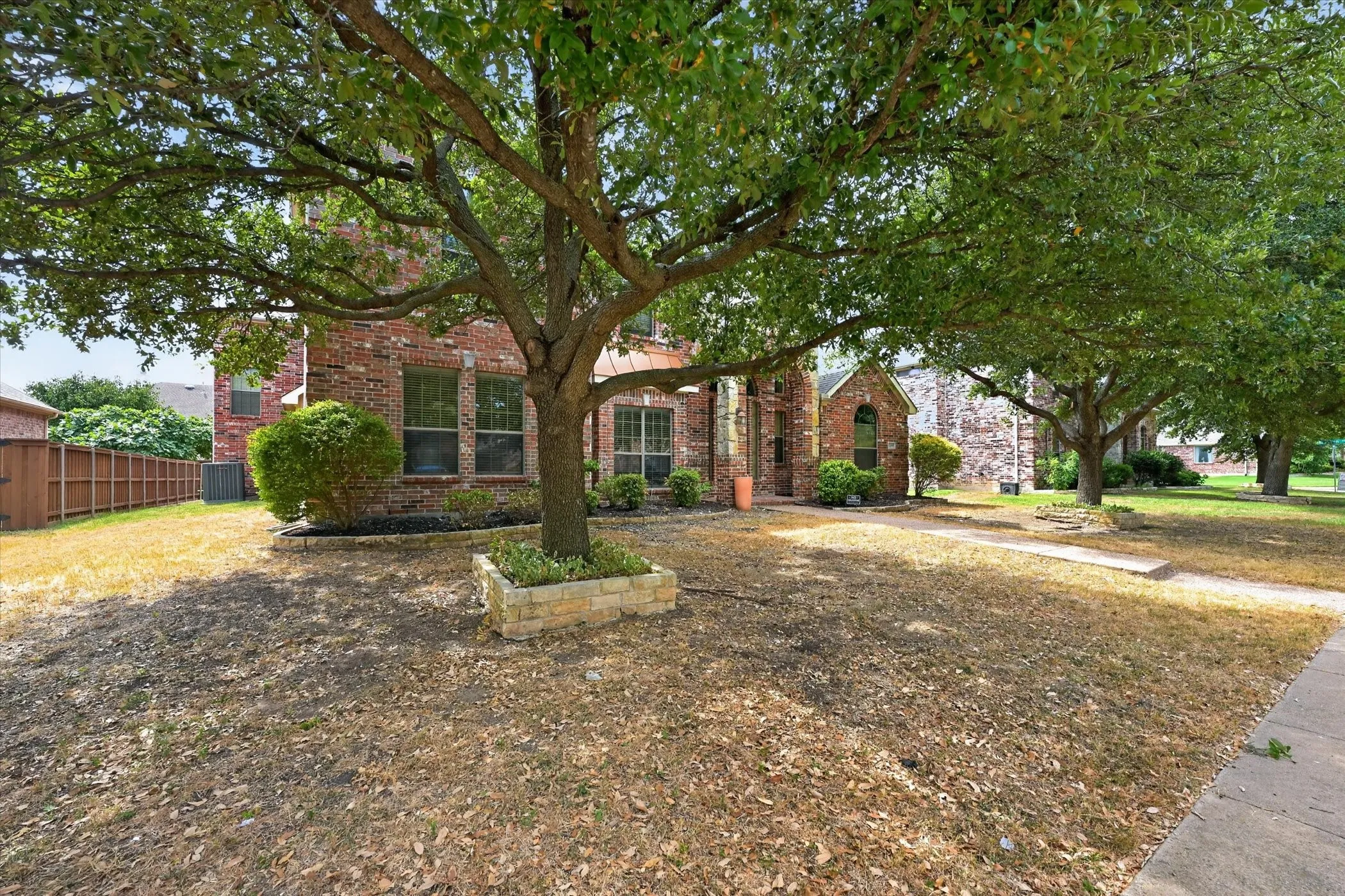 Brick exterior with multiple windows, mature trees, and a concrete walkway