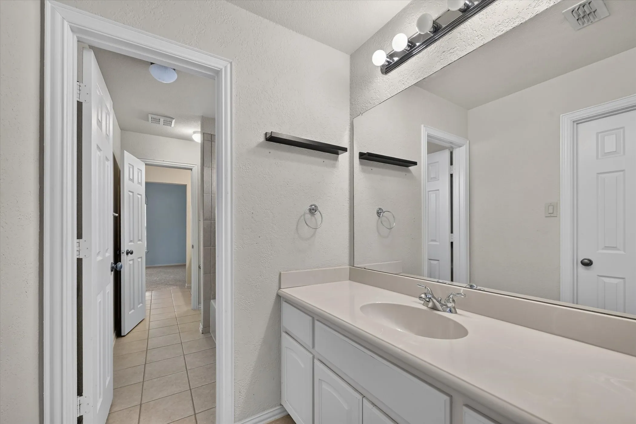 Vanity with integrated sink, chrome faucet, and expansive wall-mounted mirror