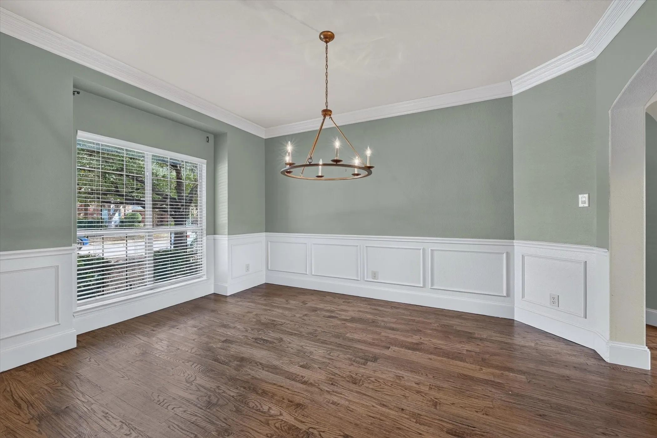 Hardwood-style flooring, wainscoting, crown molding, a large window, and an overhead chandelier