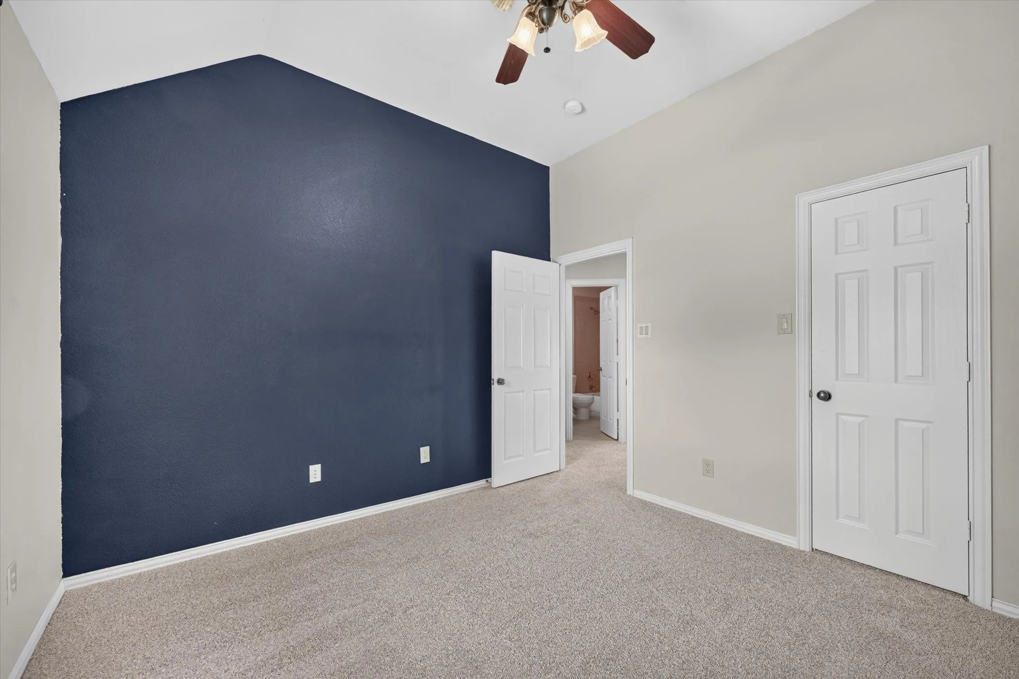 Vaulted ceiling, ceiling fan, white paneled doors, and carpet flooring