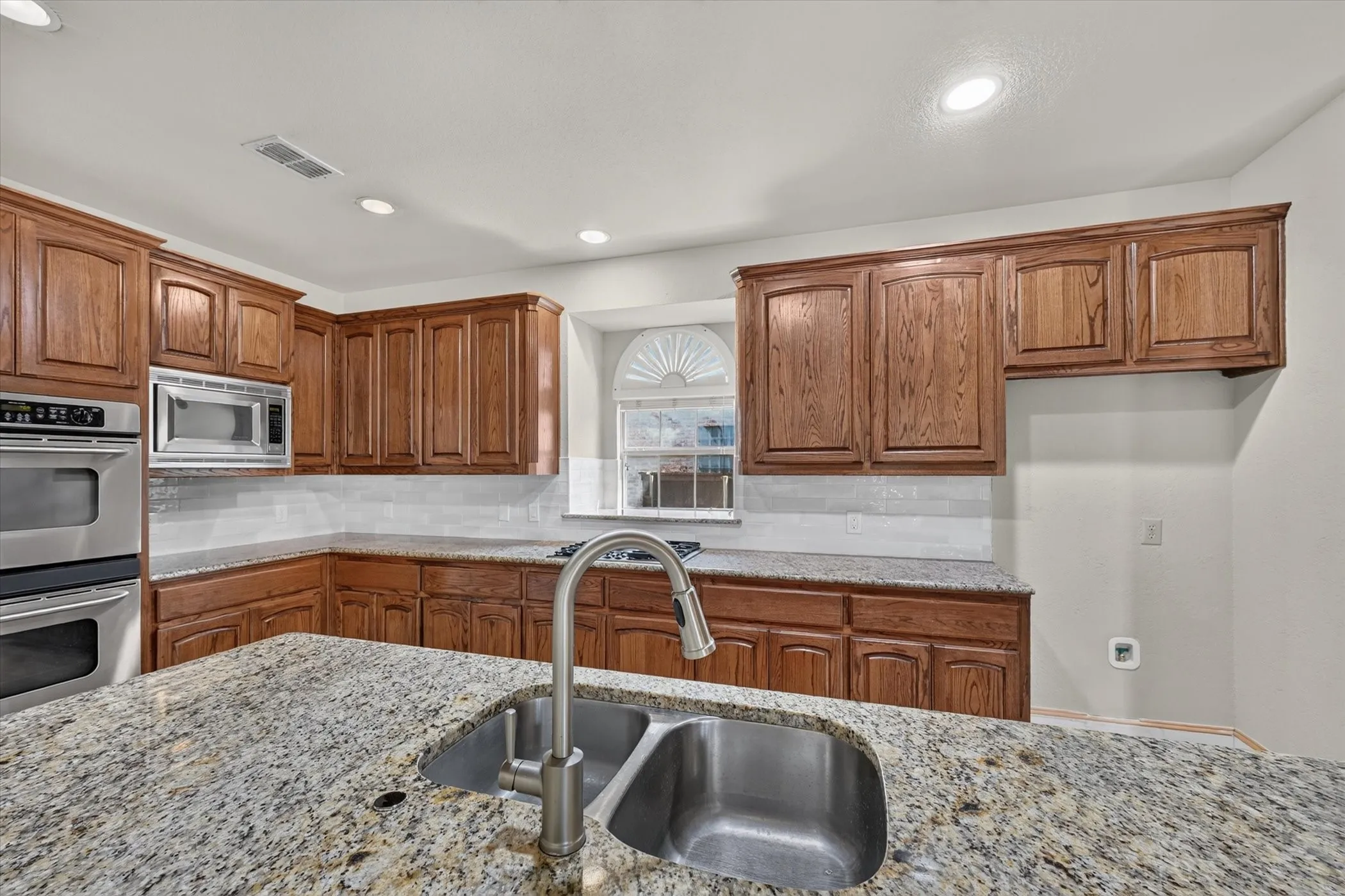 Kitchen featuring wood cabinetry, stainless steel double ovens, stainless steel microwave, light-colored backsplash, and recessed lighting