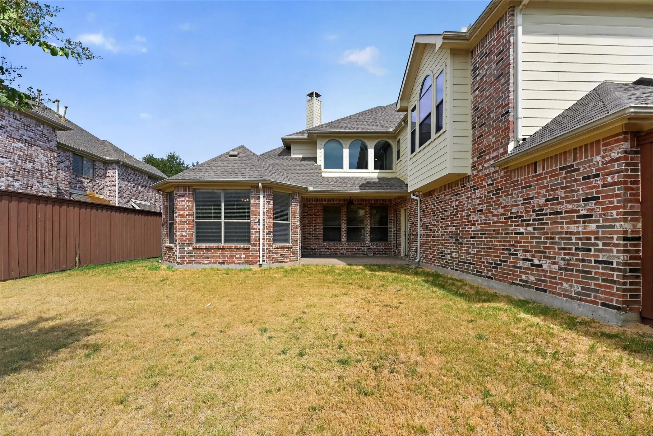 Brick and siding exterior with multiple arched windows and a ground-level patio
