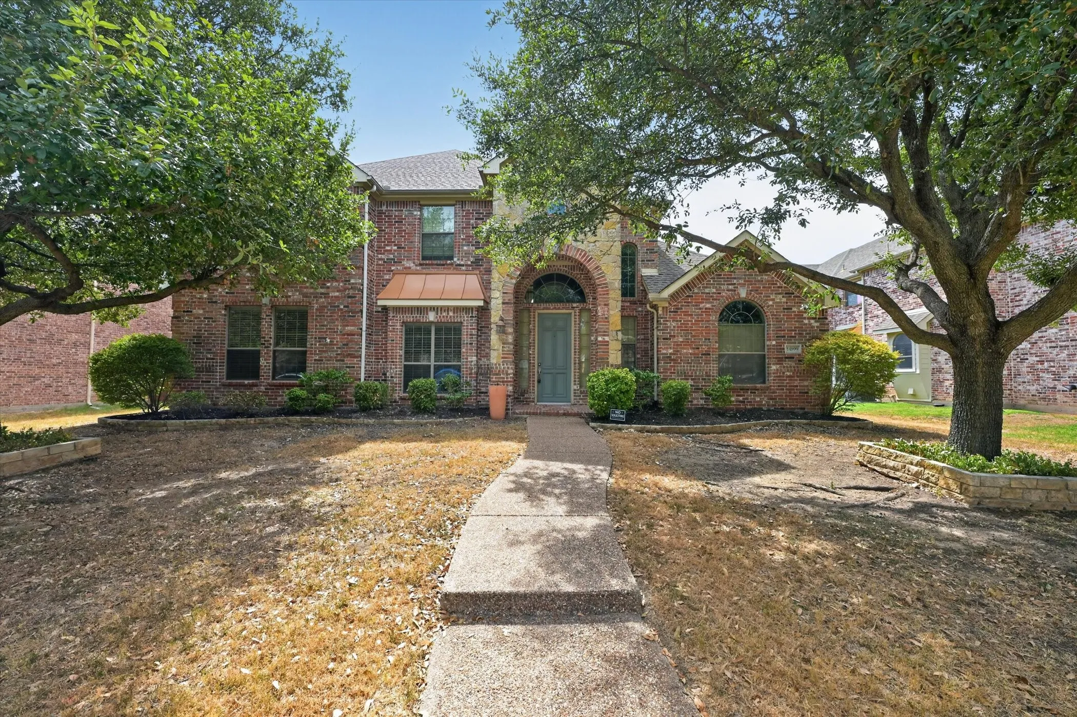 Brick facade, arched entry, copper-toned bay window awning, mature trees, and concrete walkway