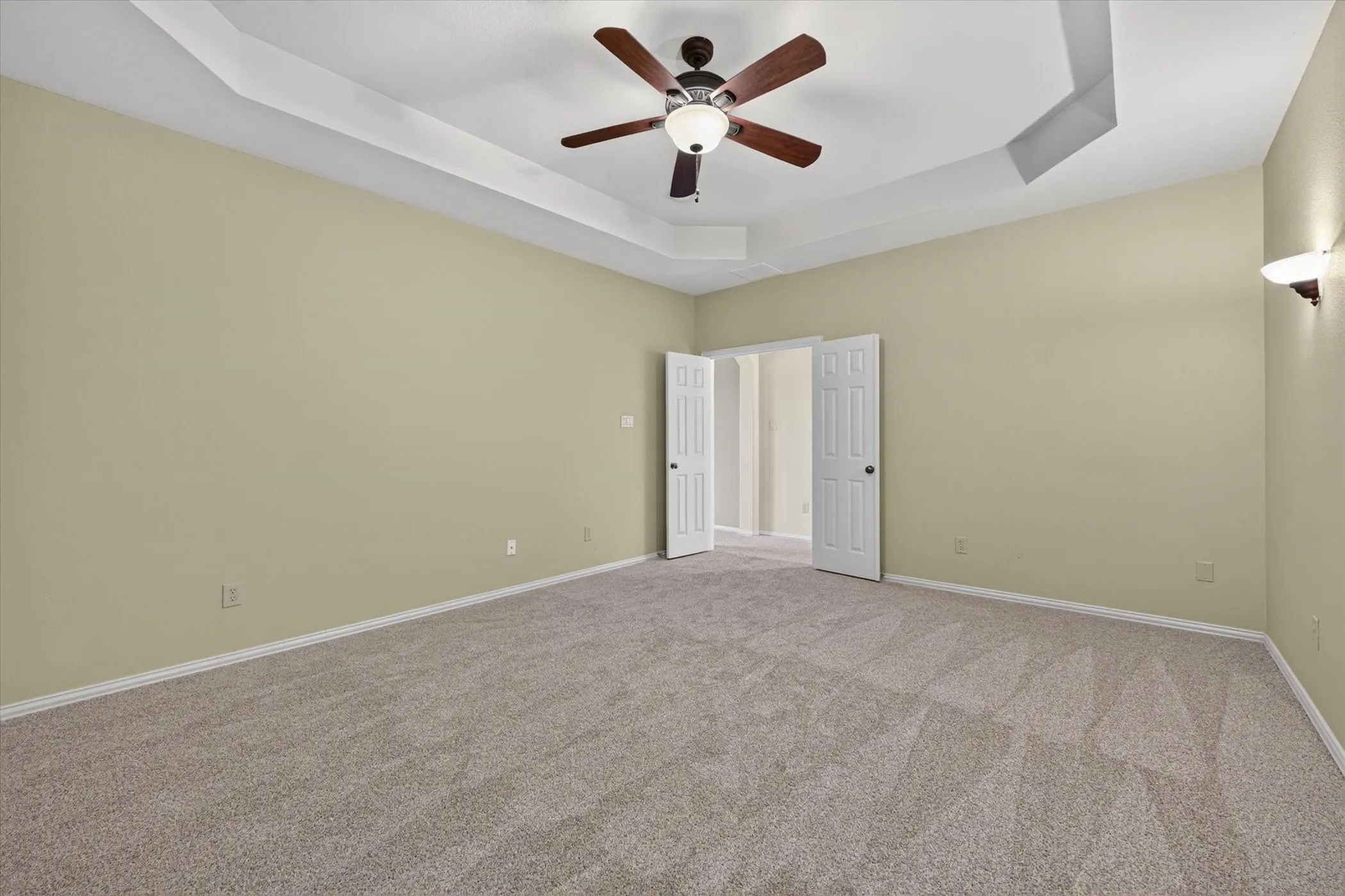 Tray ceiling with a ceiling fan, carpeted flooring, and wall sconces