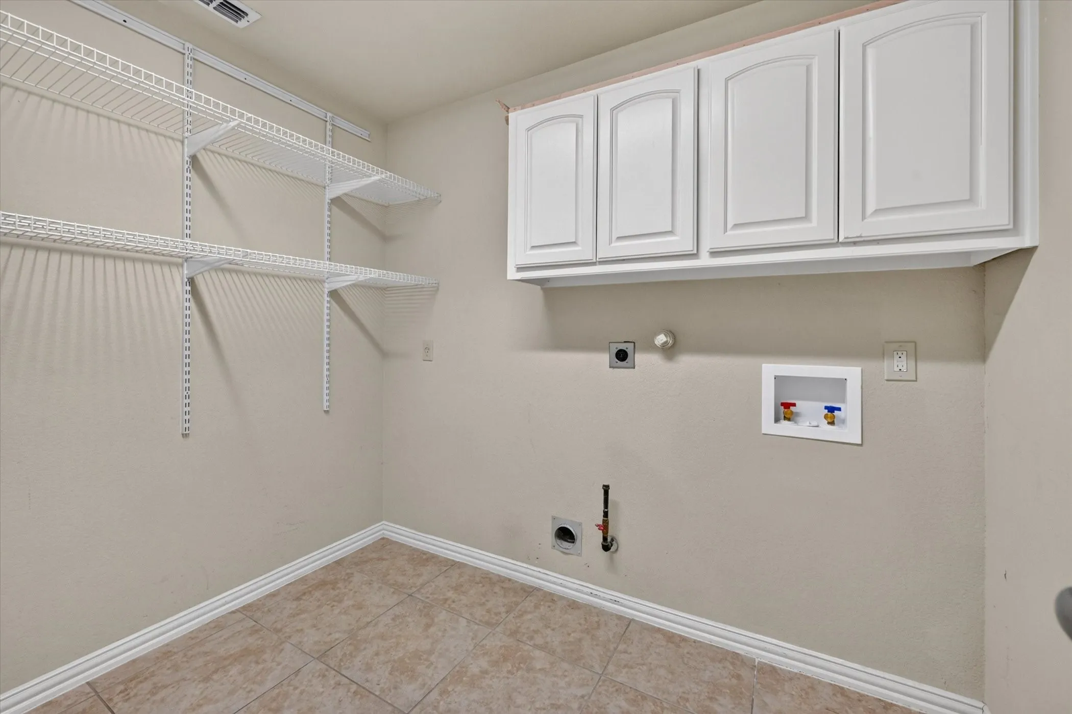 Laundry area with tile flooring, white upper cabinetry, and wire shelving