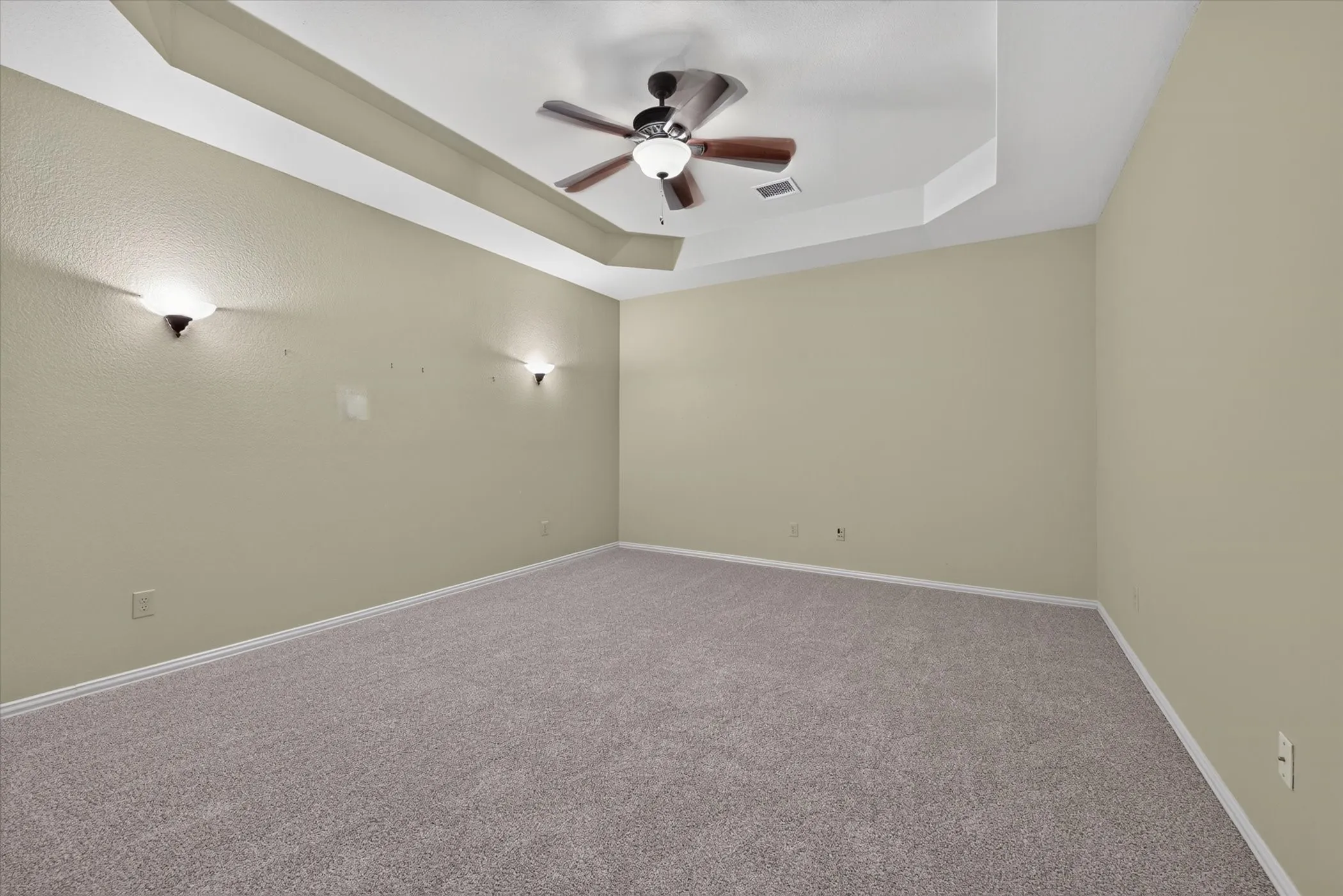 Tray ceiling with a ceiling fan, wall sconces, and carpeting