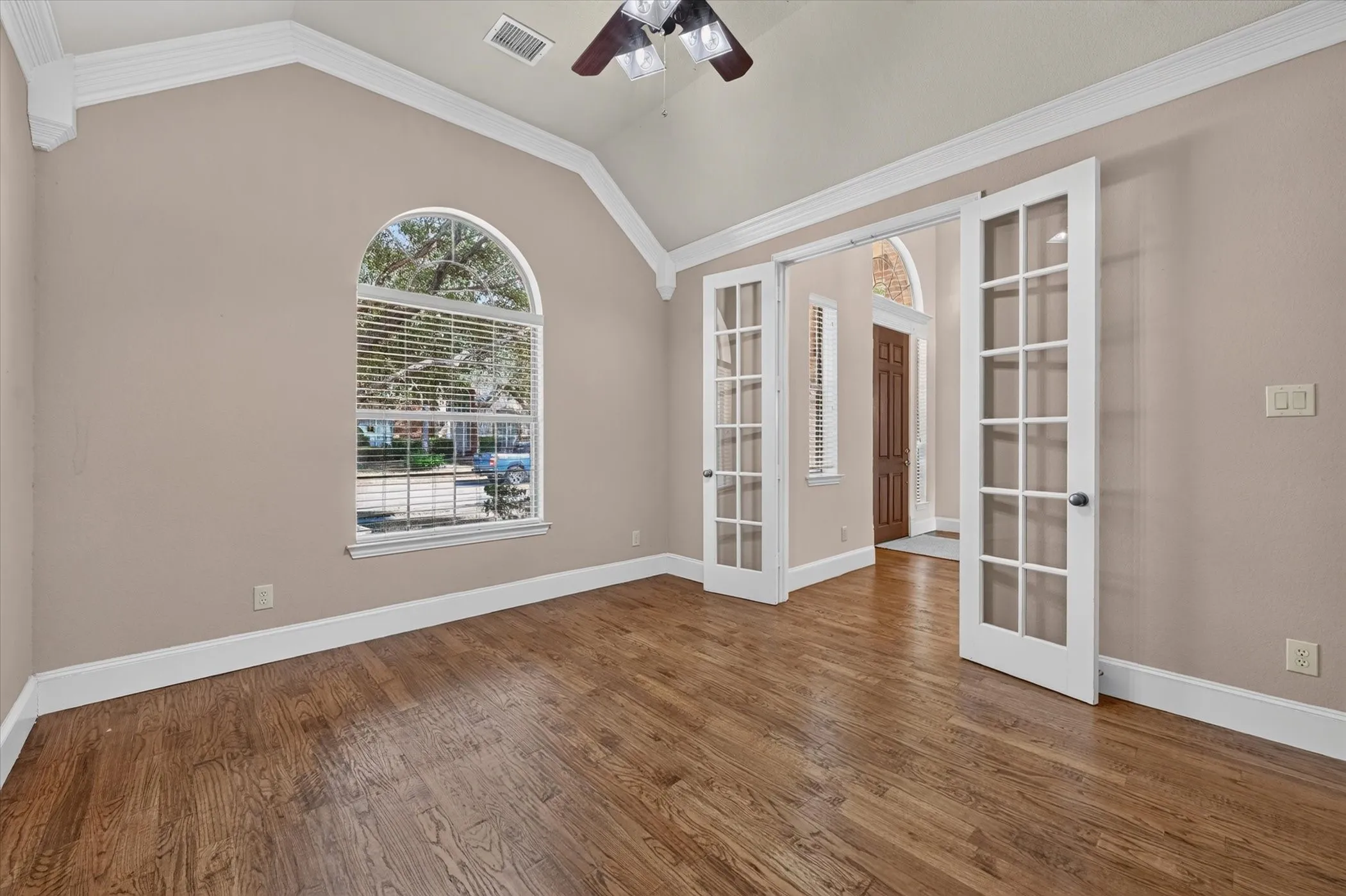 Vaulted ceiling with crown molding, hardwood flooring, arched window with horizontal blinds, and double French doors