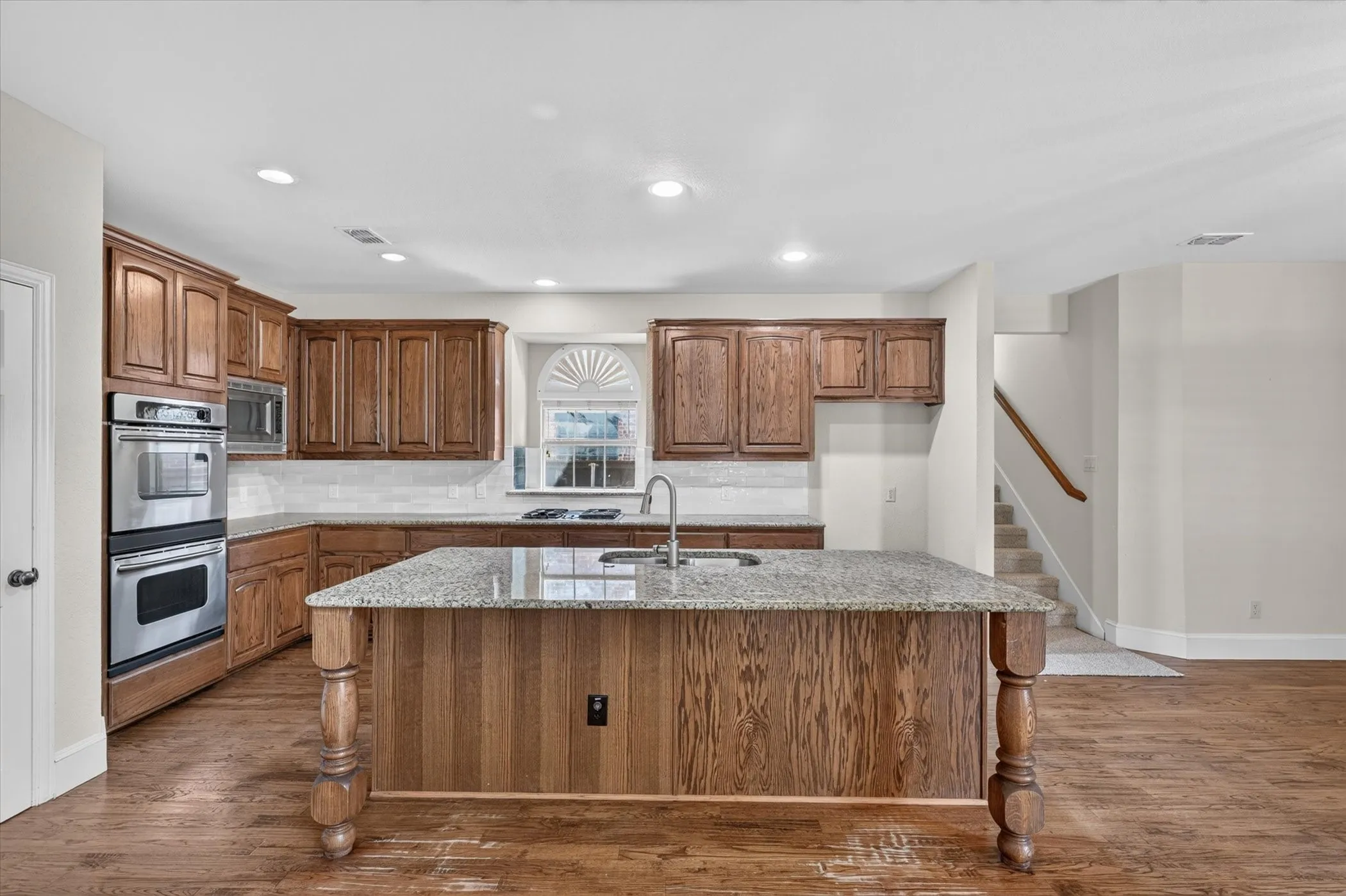 Kitchen featuring a center island, wood-finish cabinetry, stainless steel double ovens, and a tile backsplash
