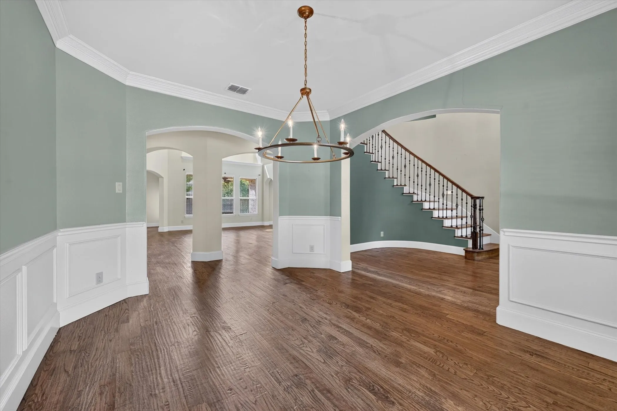 Hardwood flooring, arched doorways, wainscoting, crown molding, and a chandelier