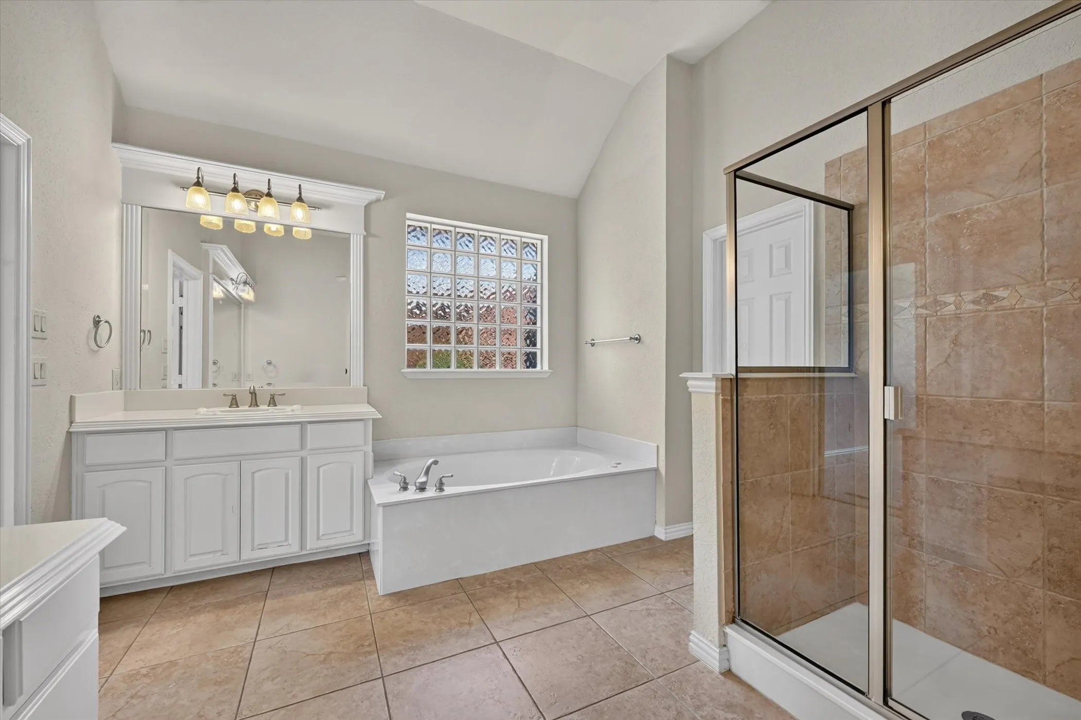 Dual vanity with white cabinetry, built-in bathtub, glass block window, and a separate tiled shower enclosure