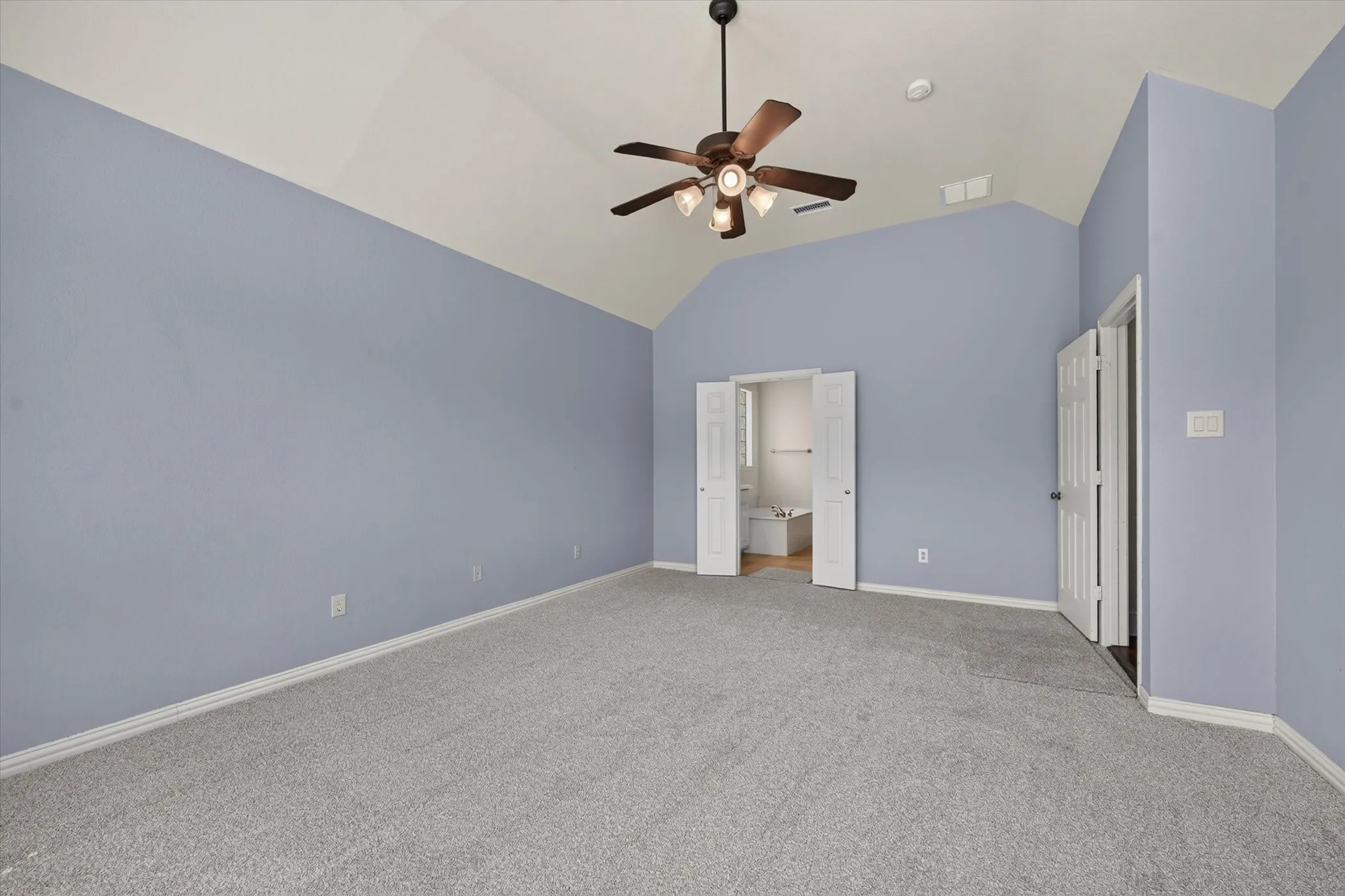 Vaulted ceiling with a ceiling fan, light gray carpeting, and an adjoining space with wood-finish flooring