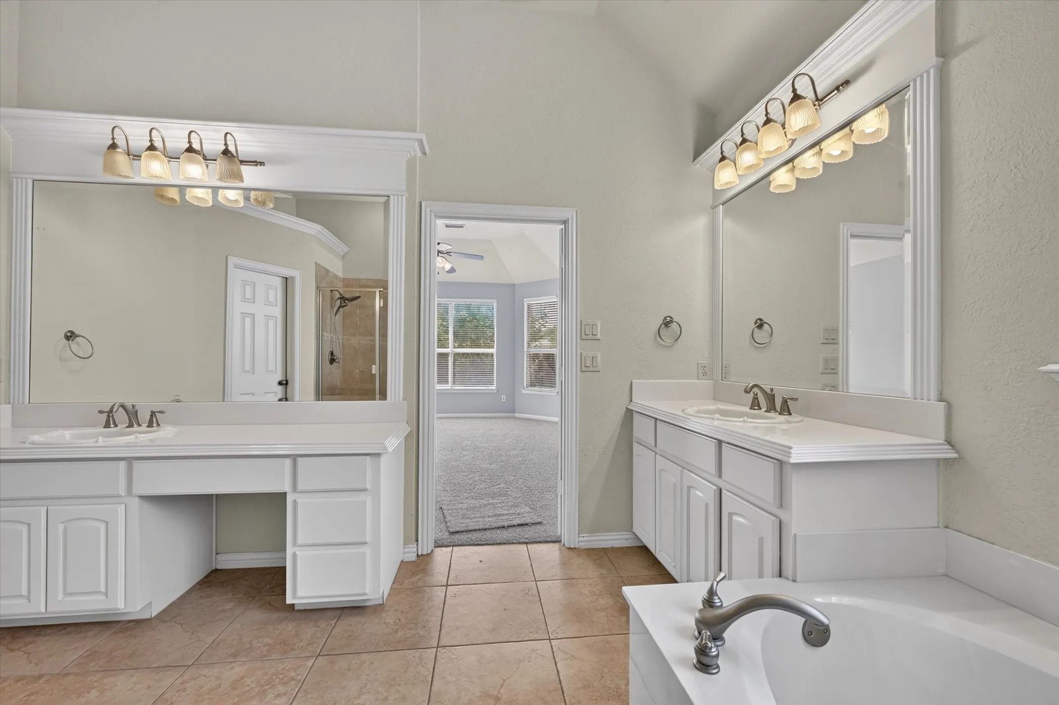 Dual vanities with integrated sinks, large mirrors, a built-in makeup area, and a corner soaking tub