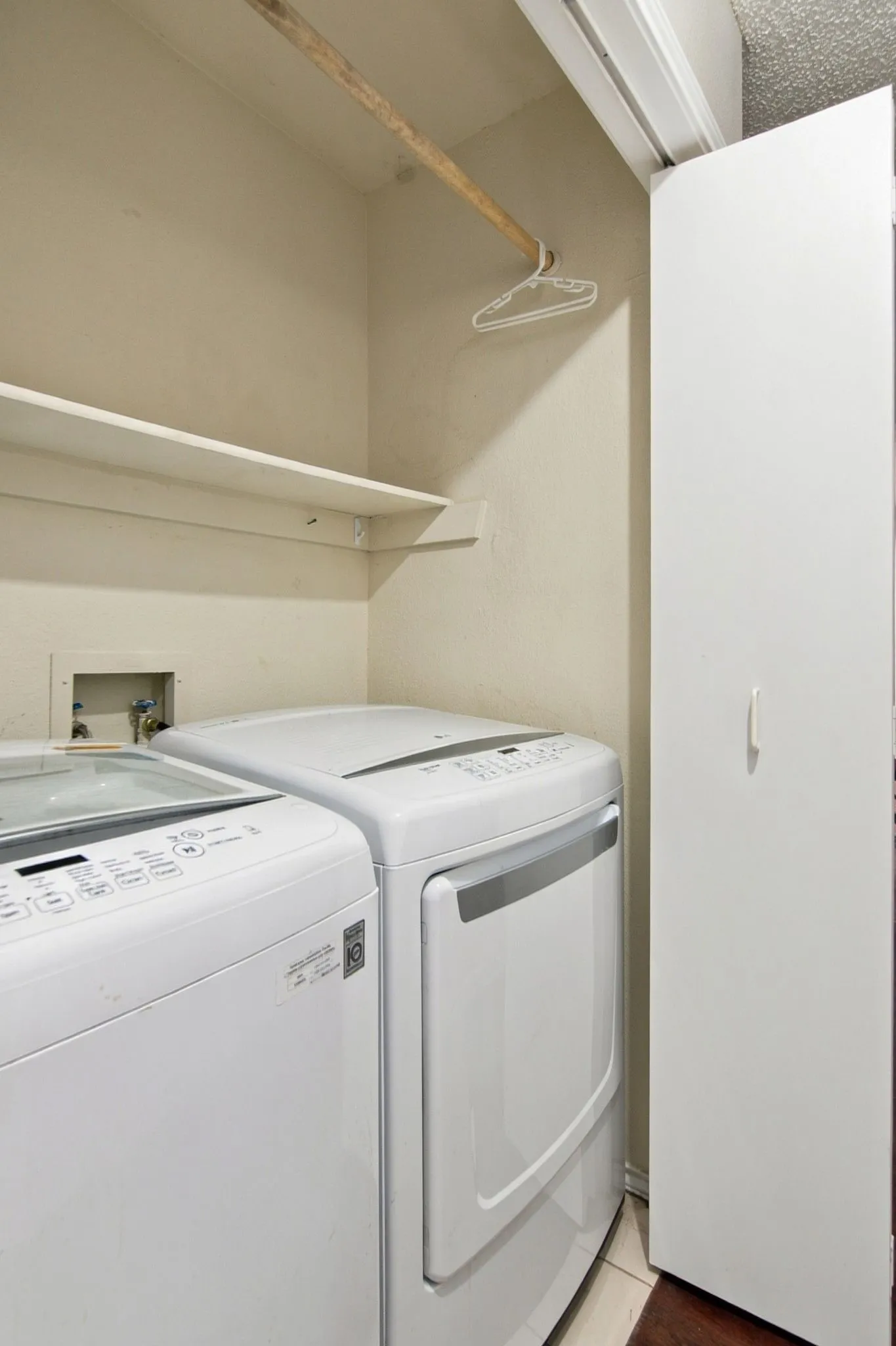 Integrated laundry closet on the first floor with white appliances, built-in shelving, and hanging rod